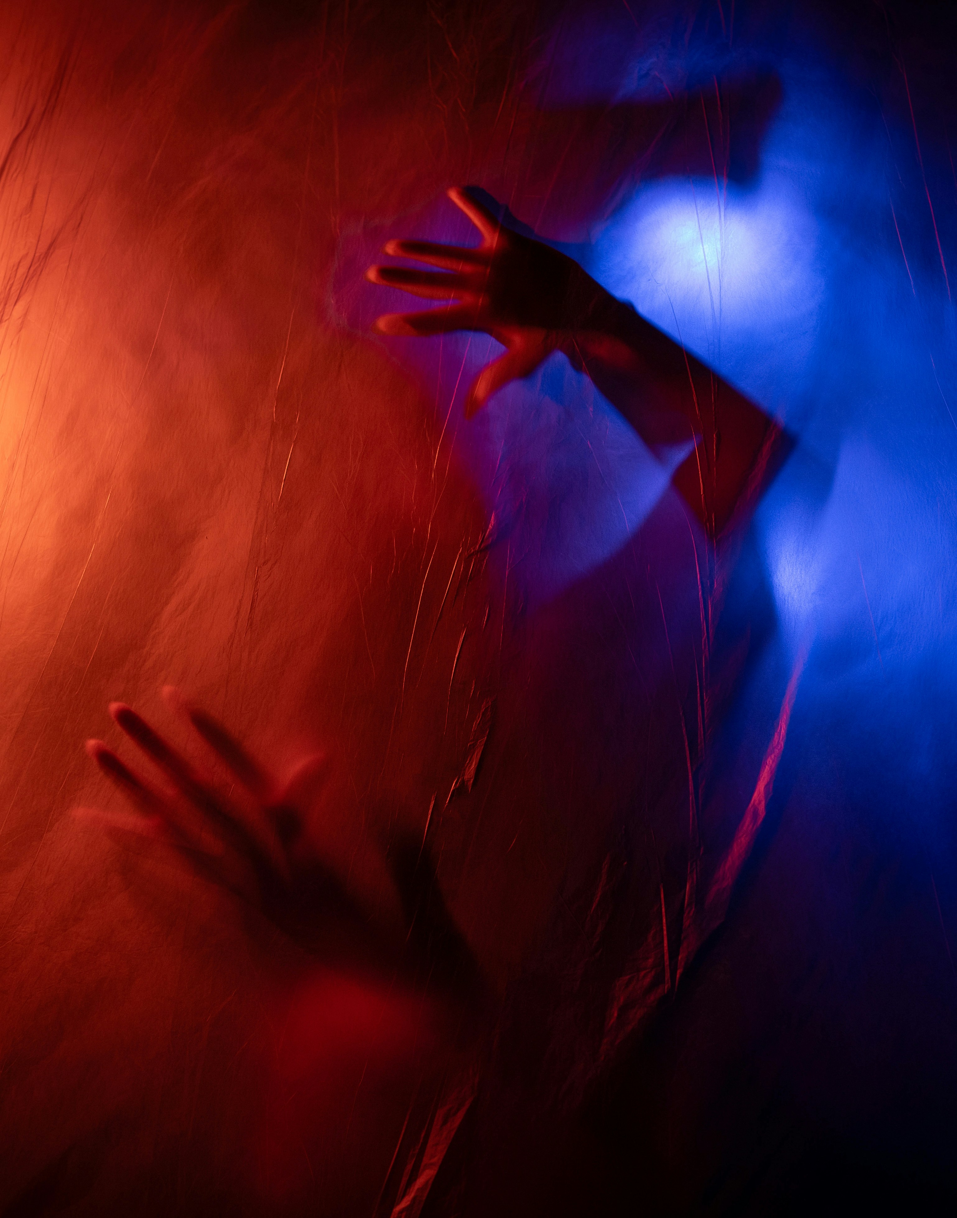 Hands pressing through red and blue illuminated fabric