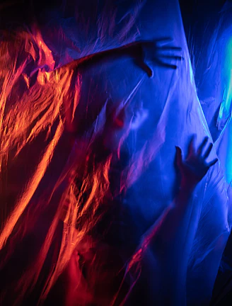 Hands reaching through wrinkled plastic sheeting with colored lights