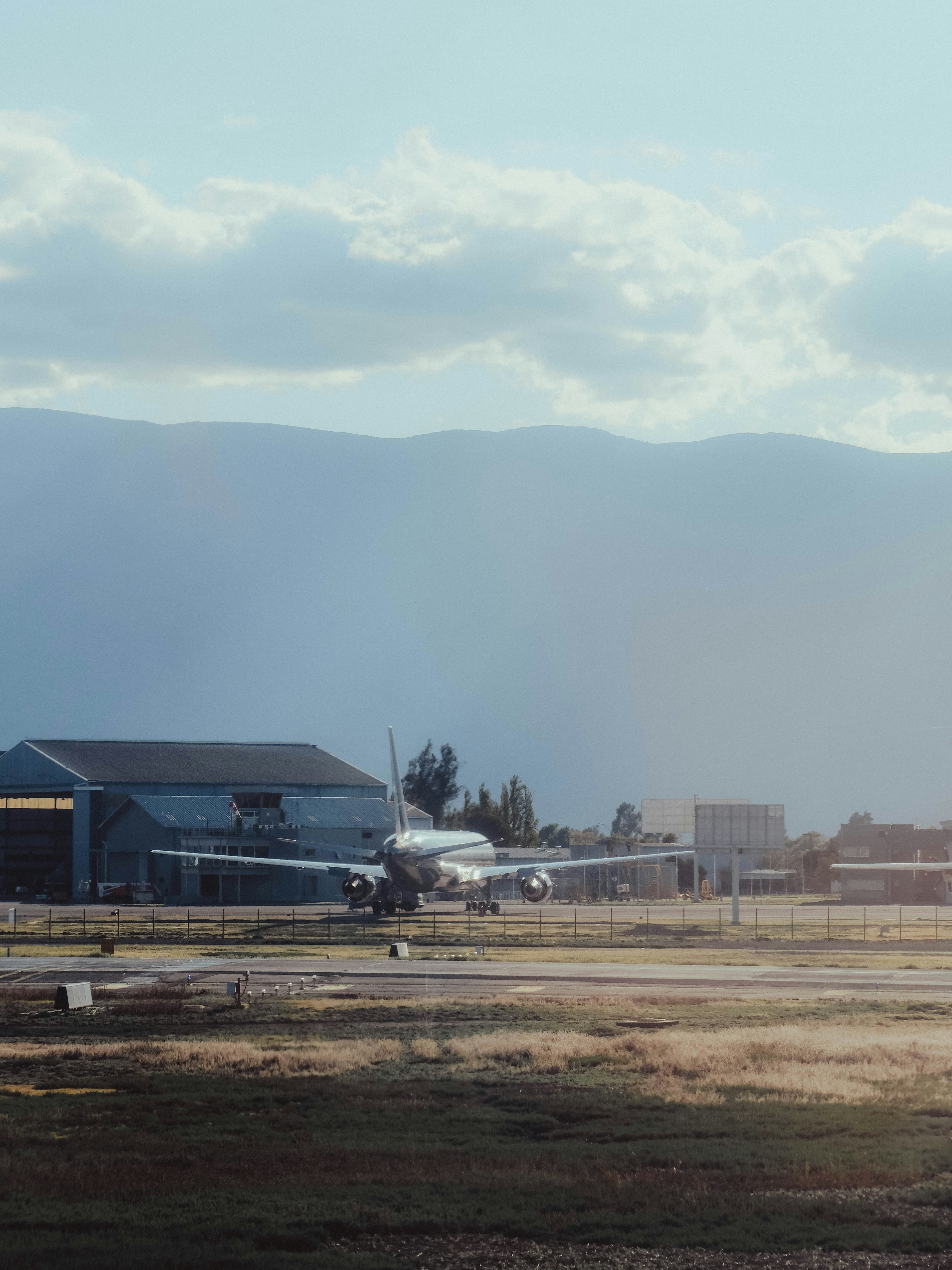 Airplane on tarmac near hangar with hangar and mountains