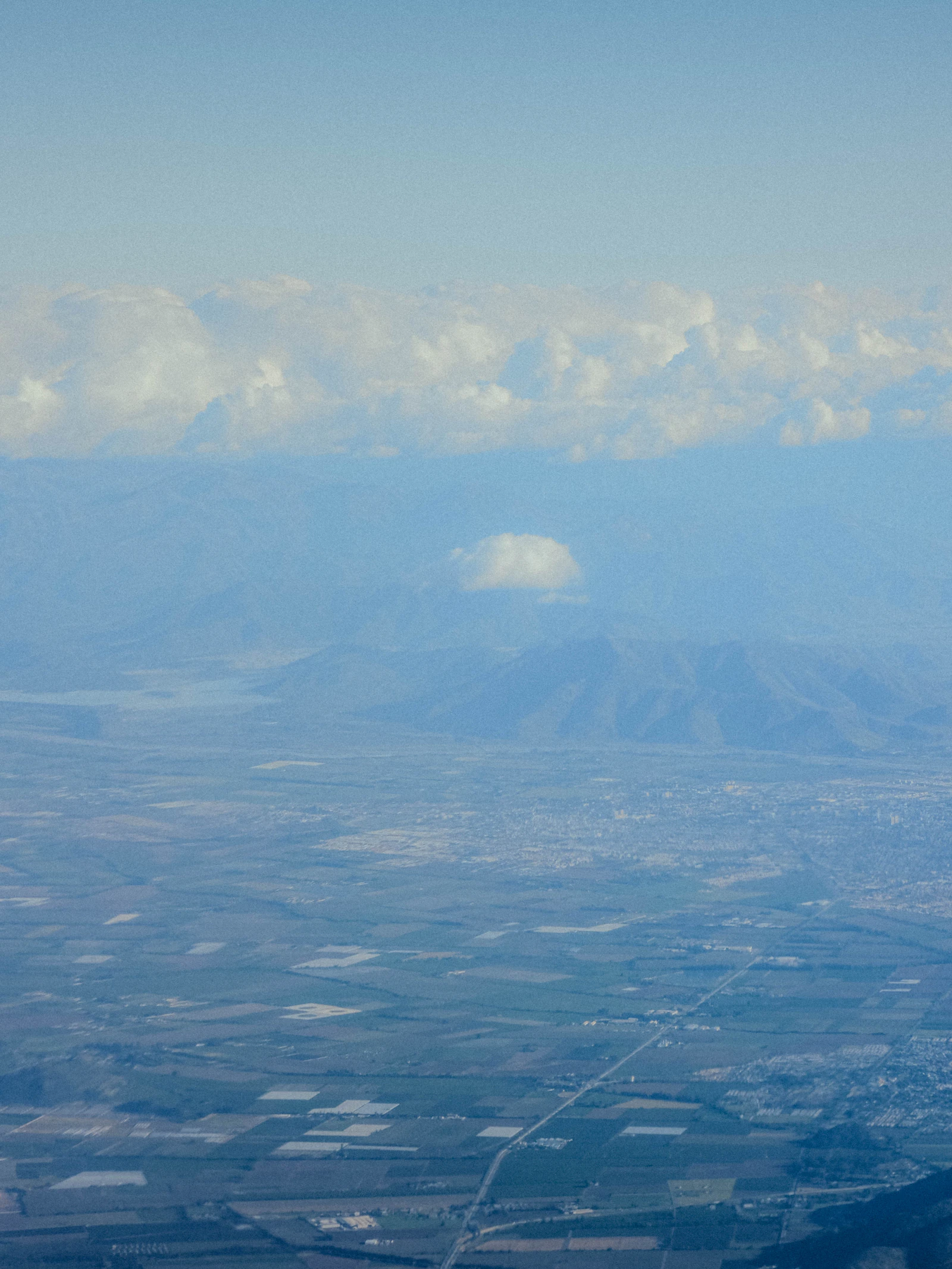 Vista aérea de un vasto paisaje con cordones de montañas y nubosidad sobre Los Lagos.