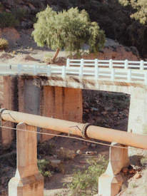 A bridge supports a large pipe over a dry landscape.
