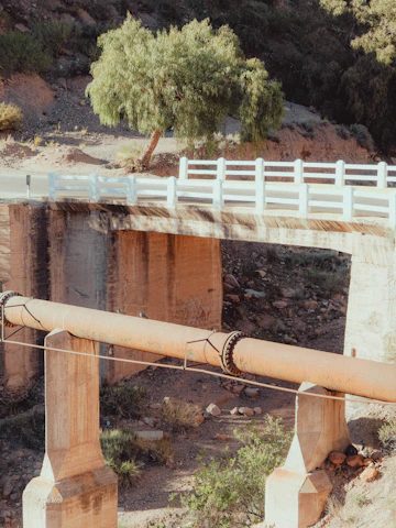 A bridge supports a large pipe over a dry landscape.