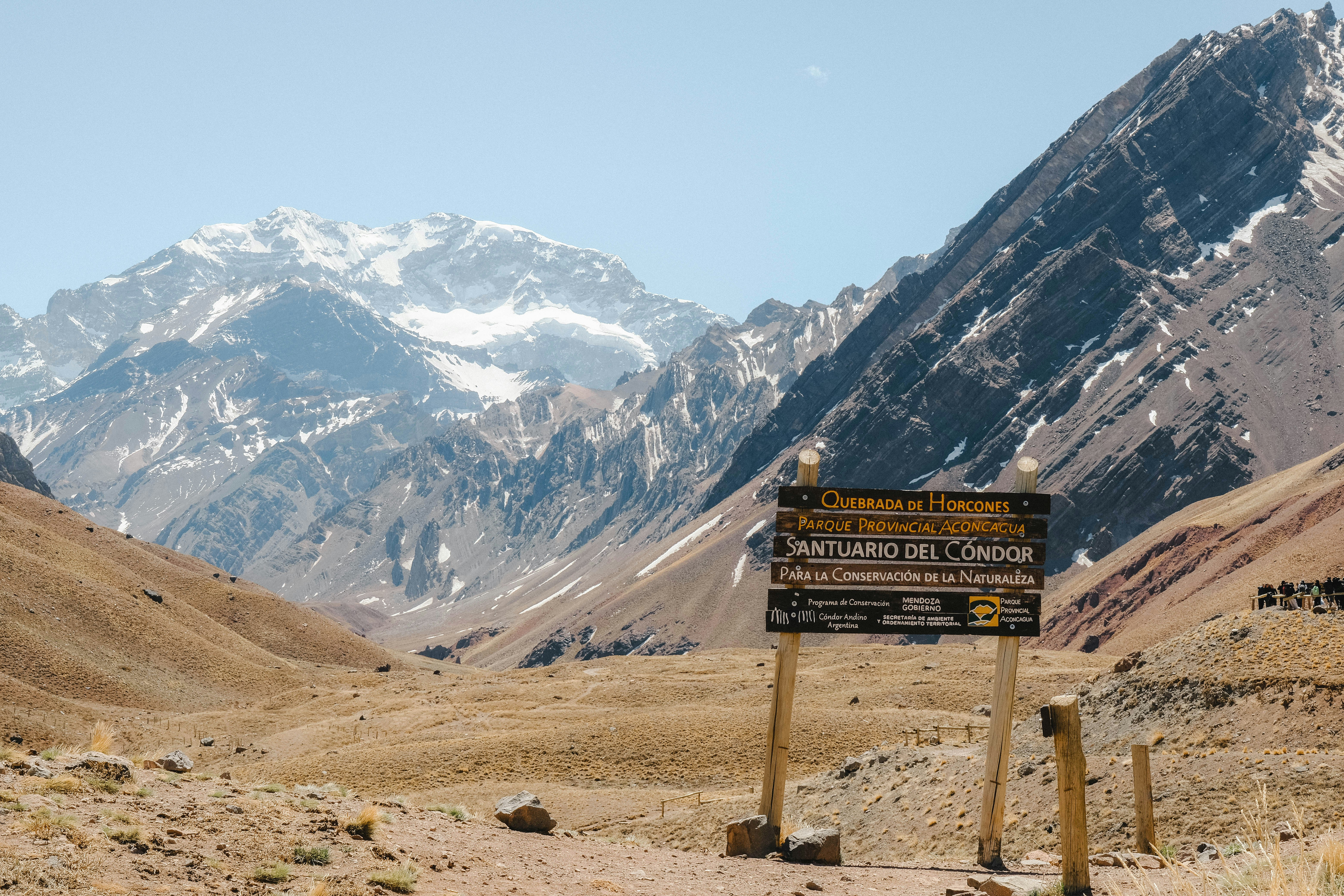 Wooden signpost in a mountain valley with snowy peaks.