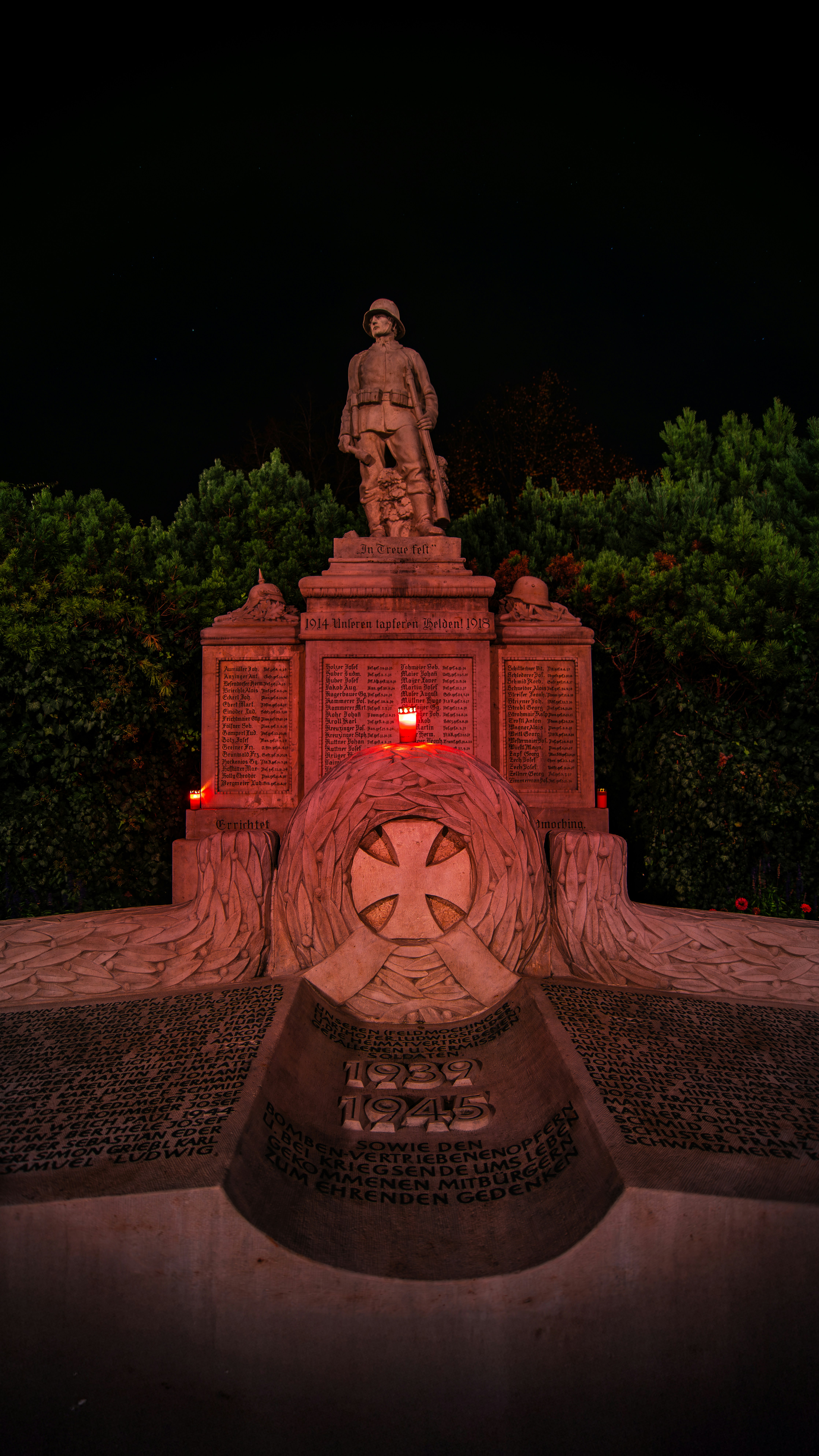Monument with soldier statue illuminated by candles at night