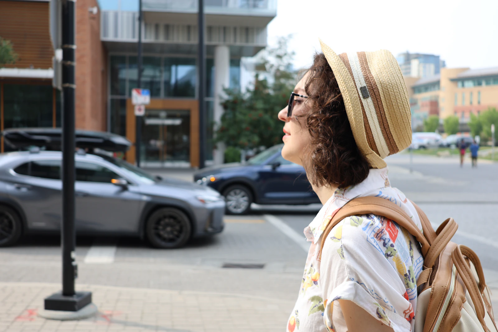 Photograph showing traveller with a small backpack looks up while walking along a city street.