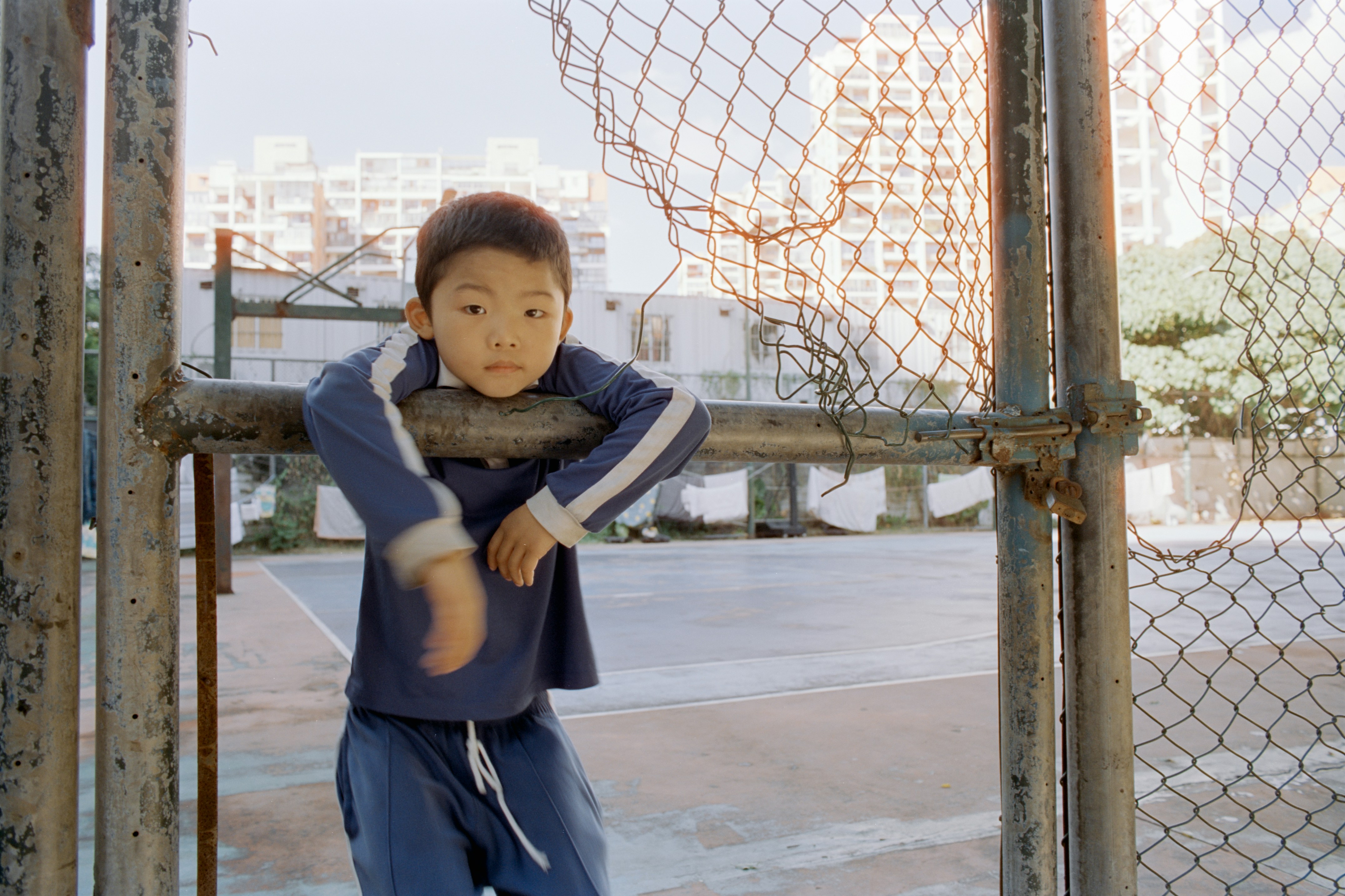 Young boy leaning on a metal fence outdoors