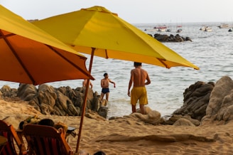 People relaxing on a rocky beach under umbrellas.
