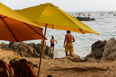 People relaxing on a rocky beach under umbrellas.