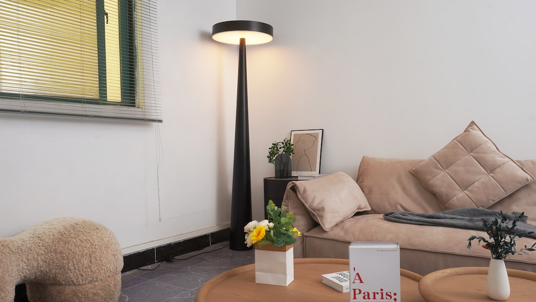 Modern black floor lamp casting warm amber light in a cozy apartment living room with beige bouclé sofa, round coffee table, and framed art print