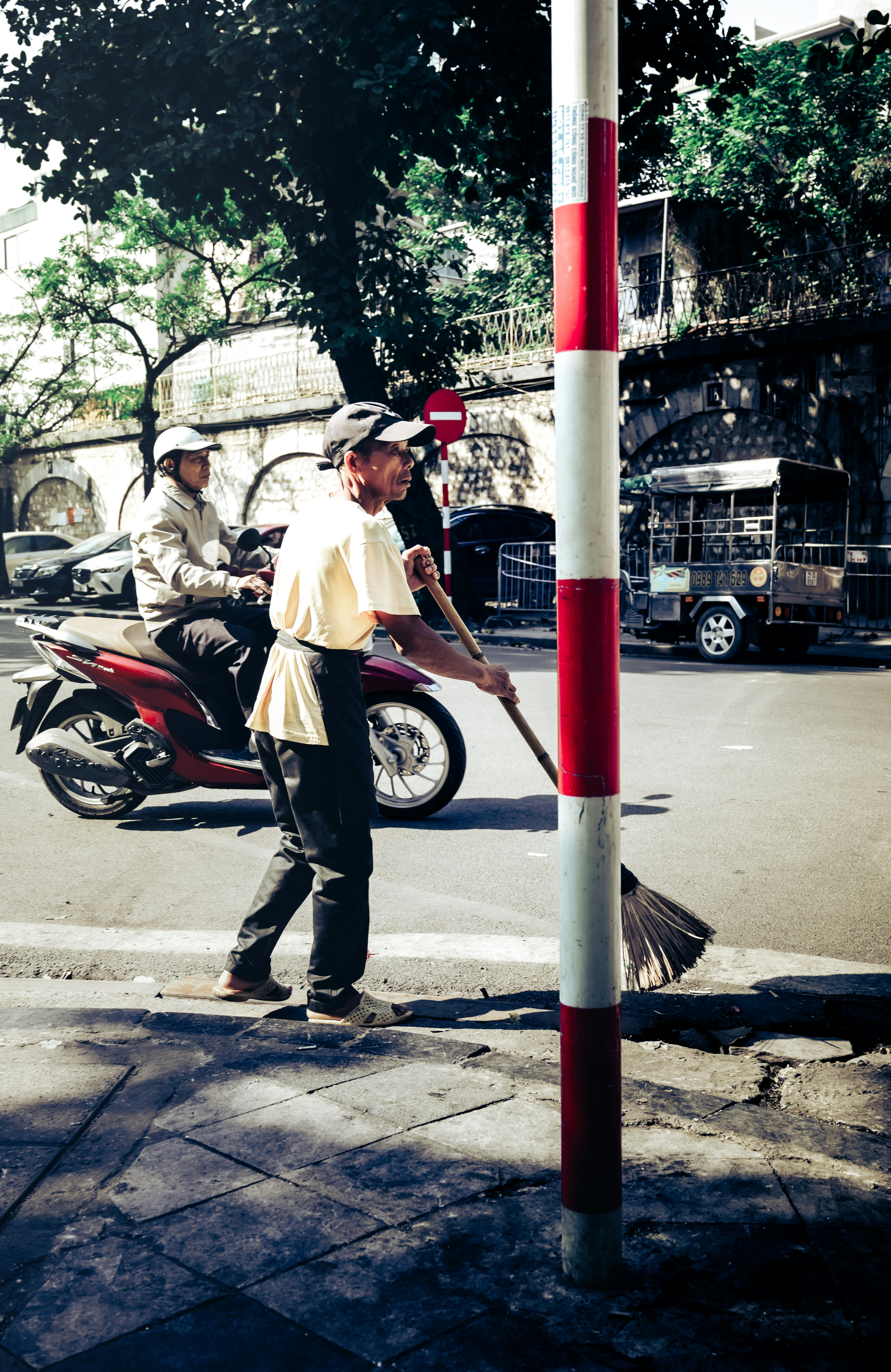 Man sweeping street next to red and white pole.