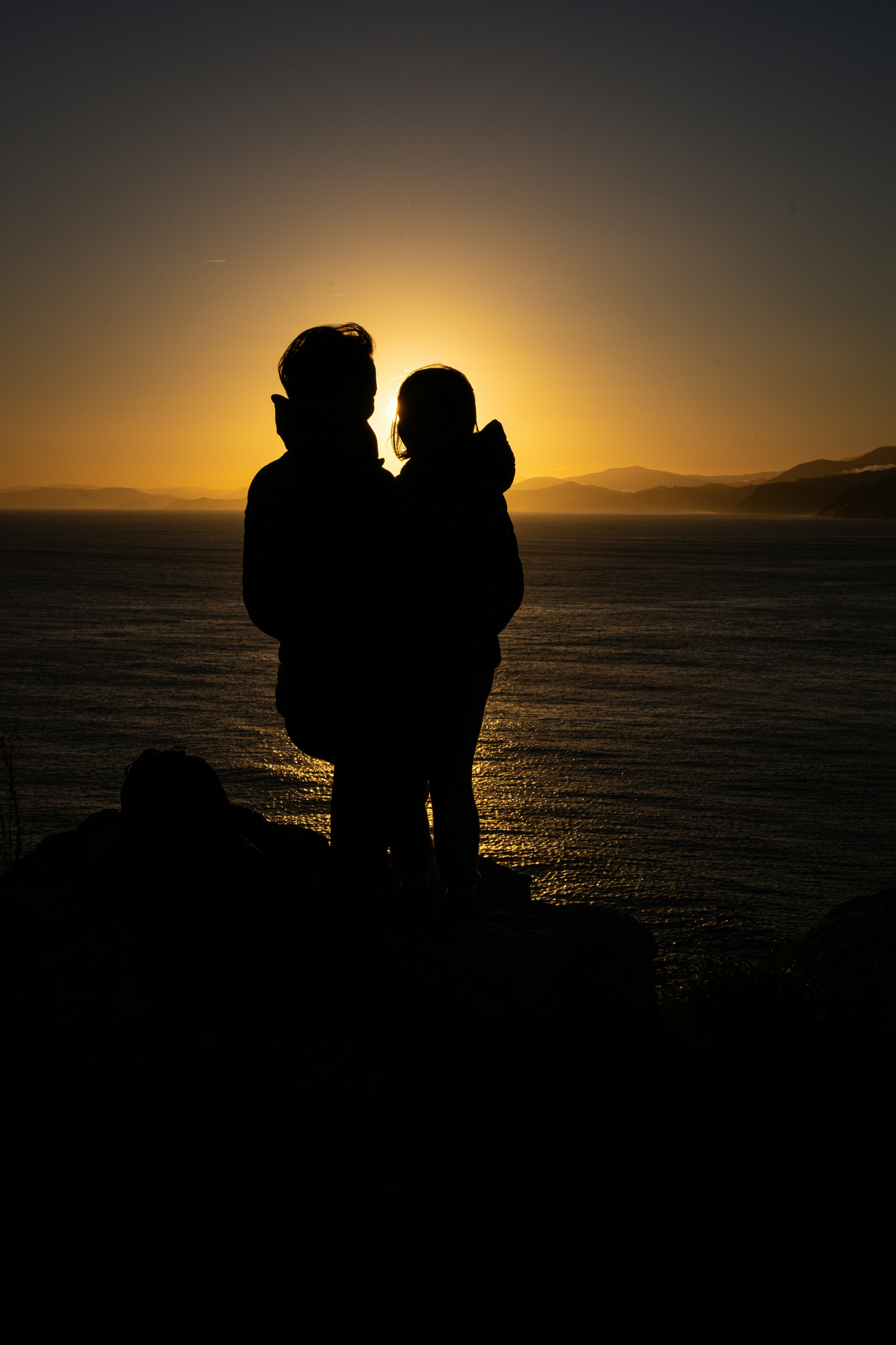 Two people silhouetted against a sunset over the ocean.