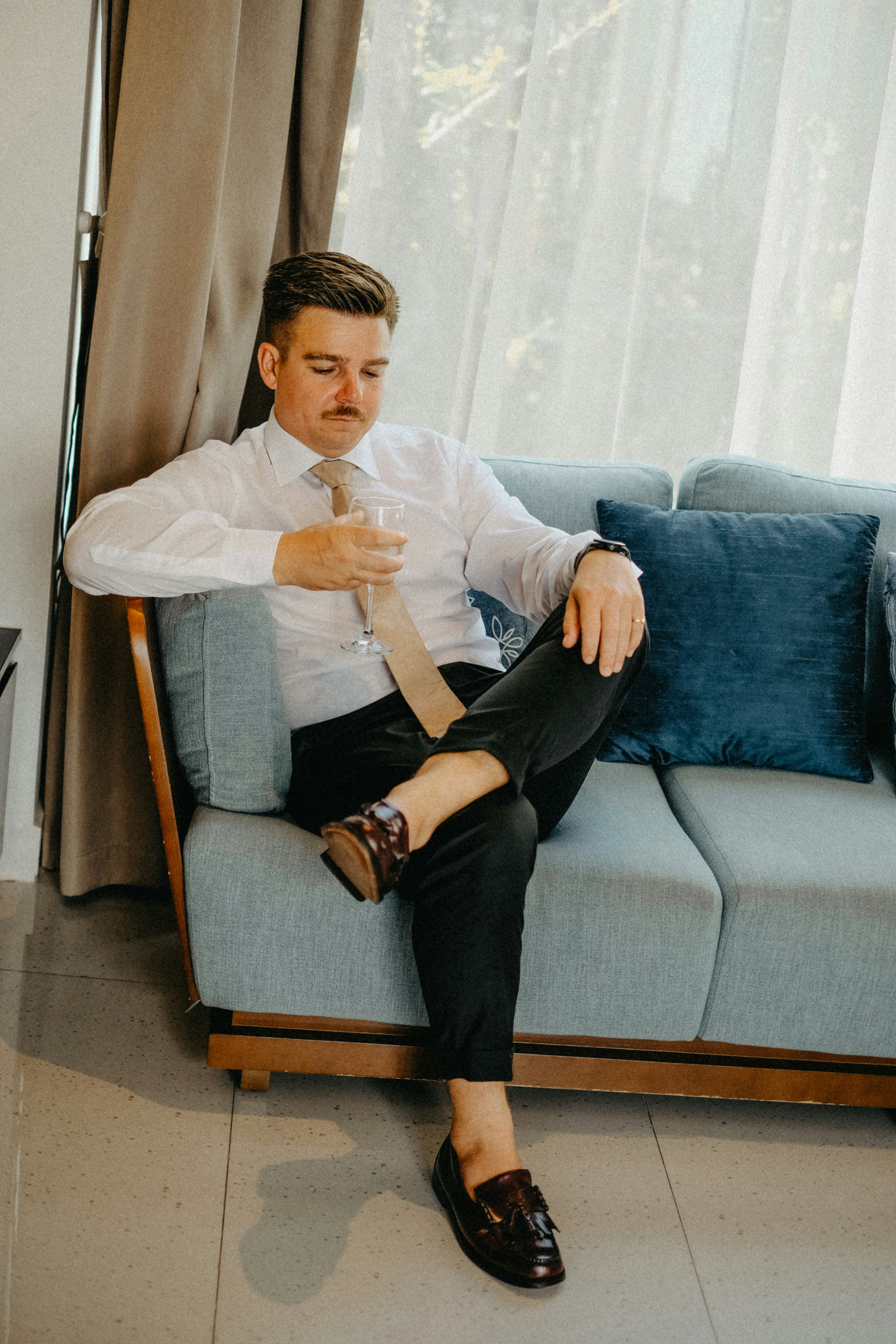 Man in white shirt and tie sitting on couch.