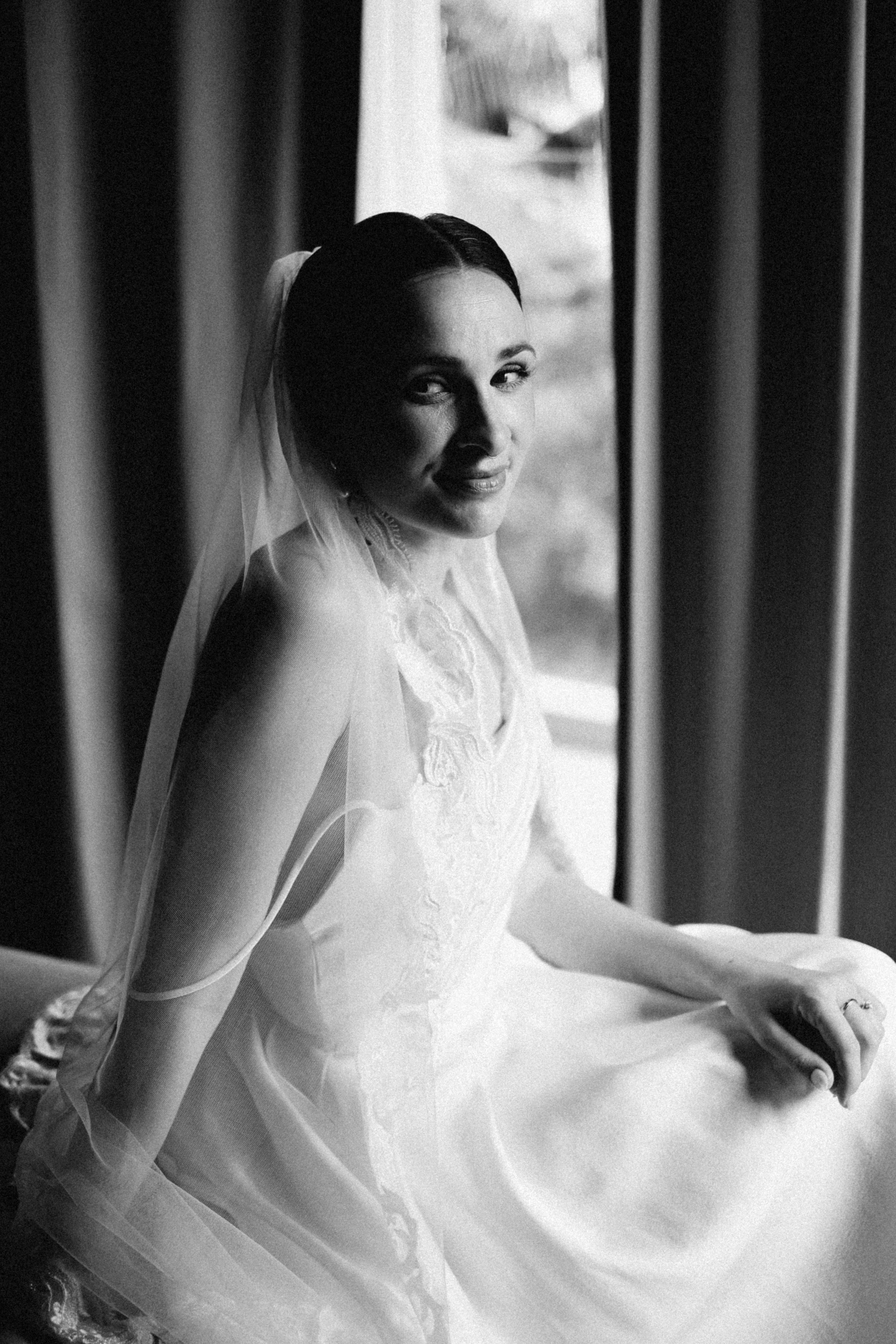 Bride in a wedding dress with veil smiling by window