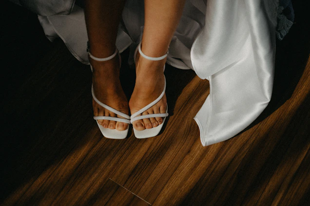 Bride's feet in white strappy heels on wooden floor.