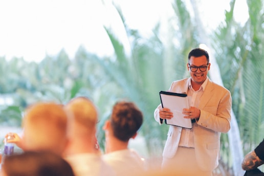 Man in suit holding clipboard speaking to audience with confidence