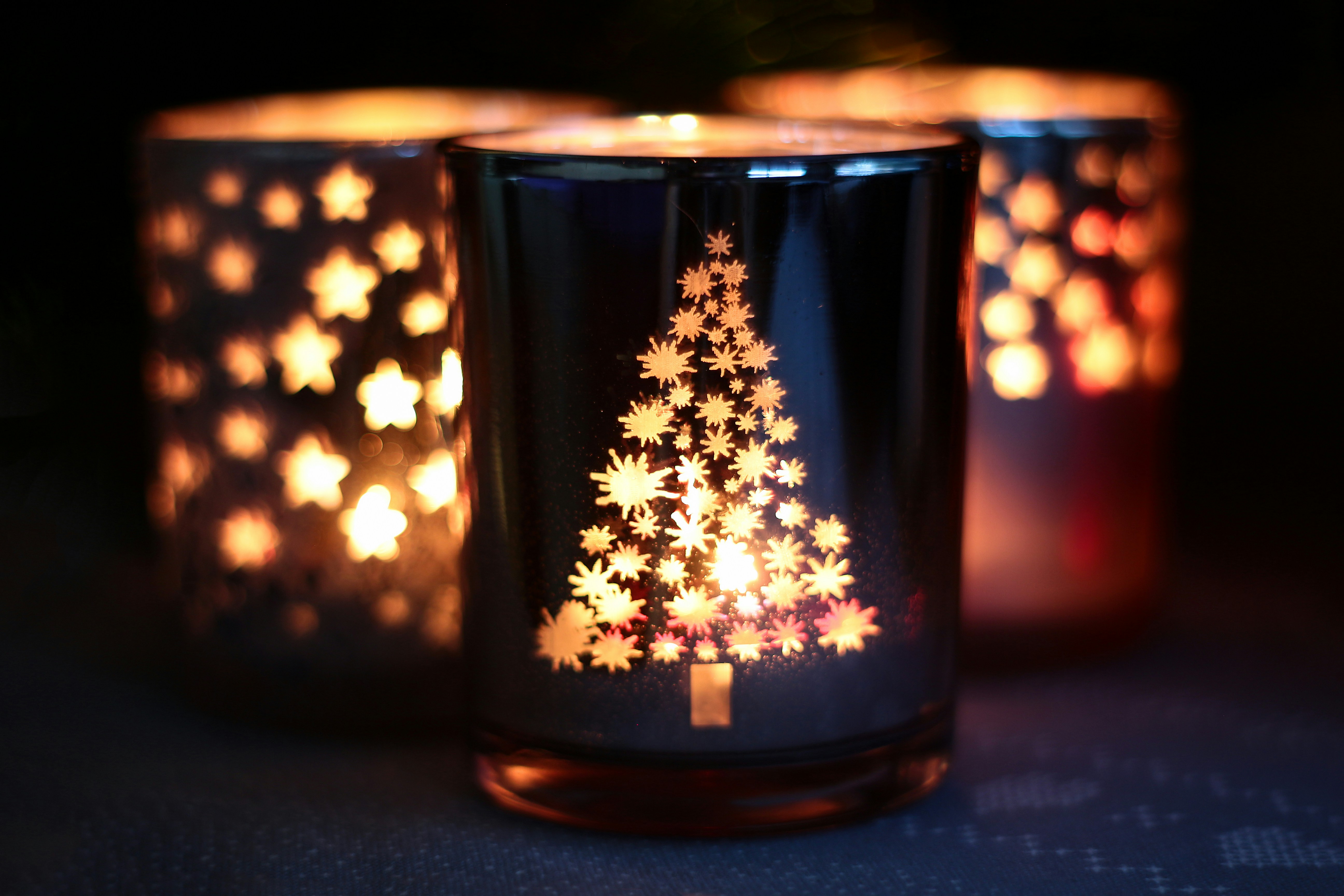 Three illuminated christmas candle holders with festive designs.