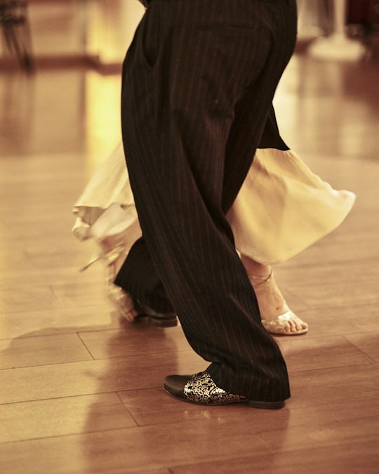 Un couple de danseurs en tenue de compétition enchaîne une figure de danse de salon sur un parquet en bois