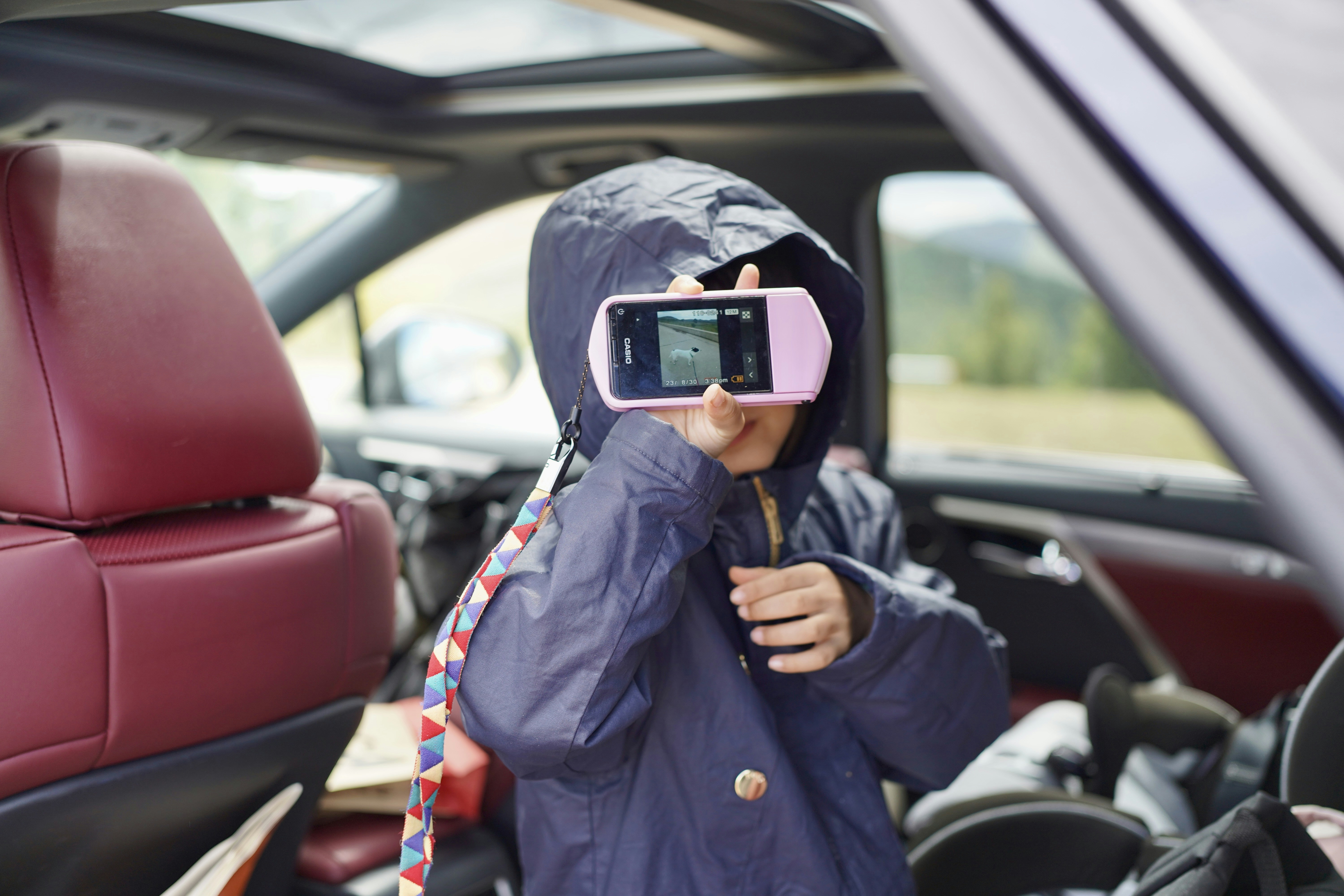 Child in raincoat taking picture with pink camera