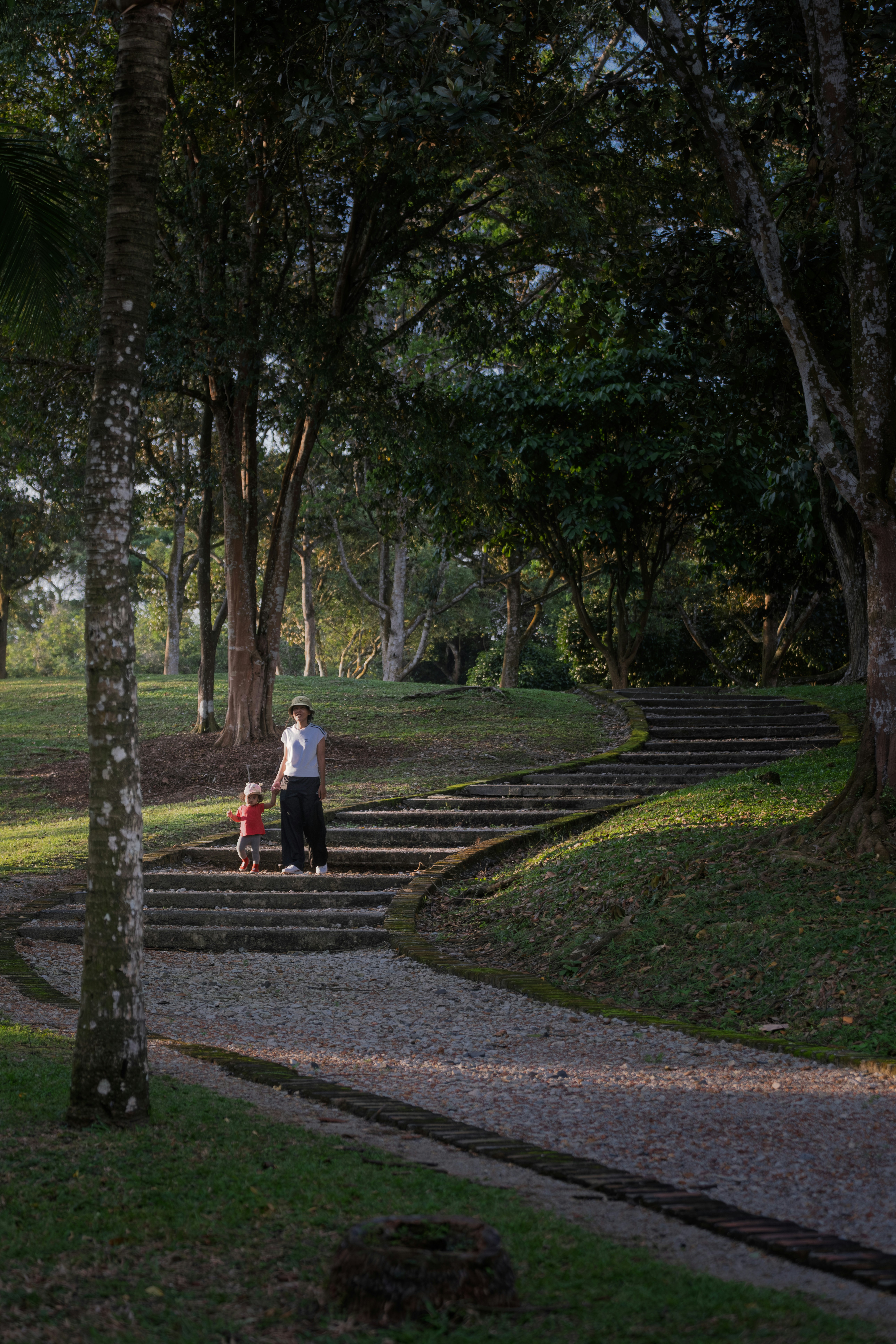 Adult and child walk up stone stairs in park.