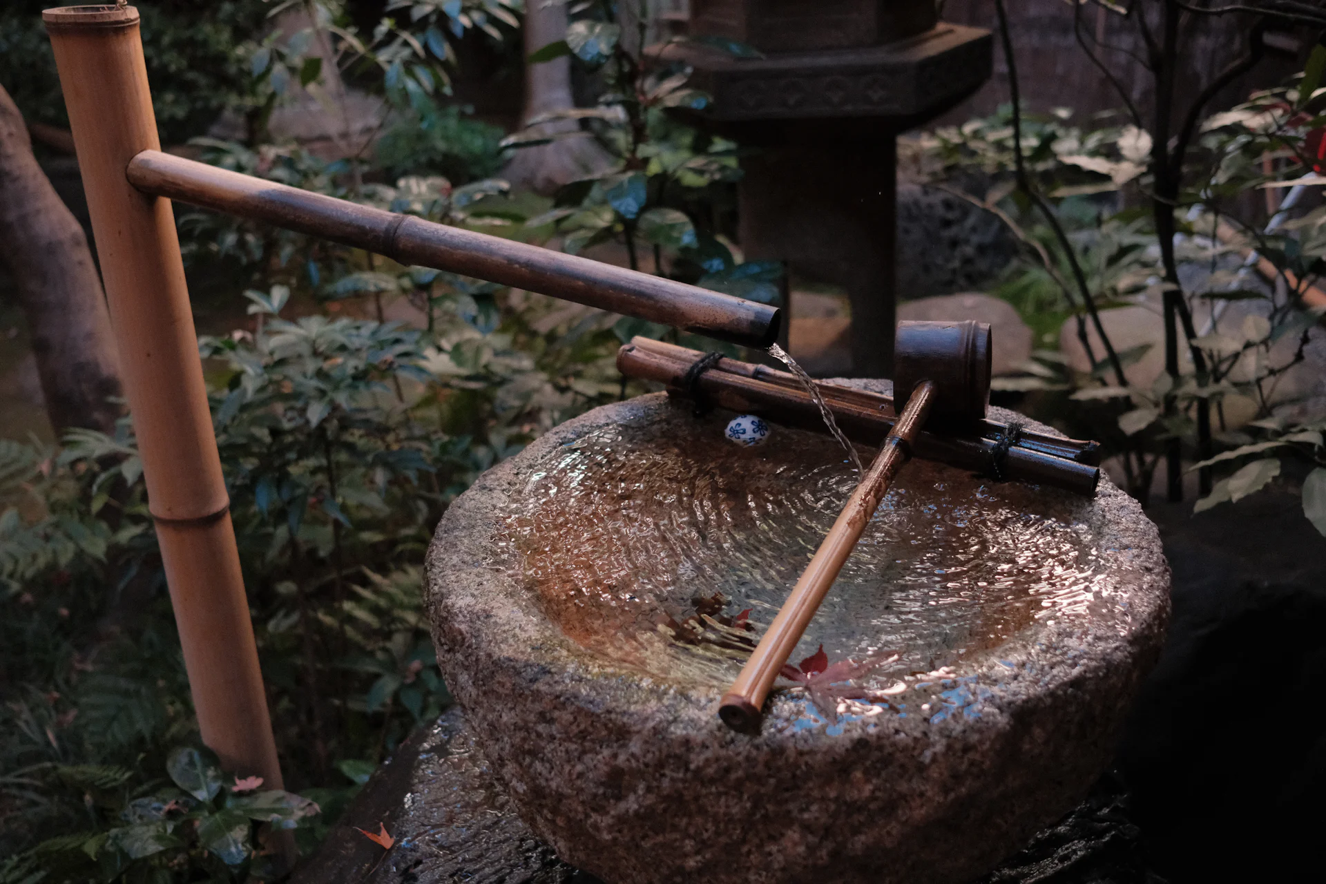Stone water basin with a bamboo spout in a garden