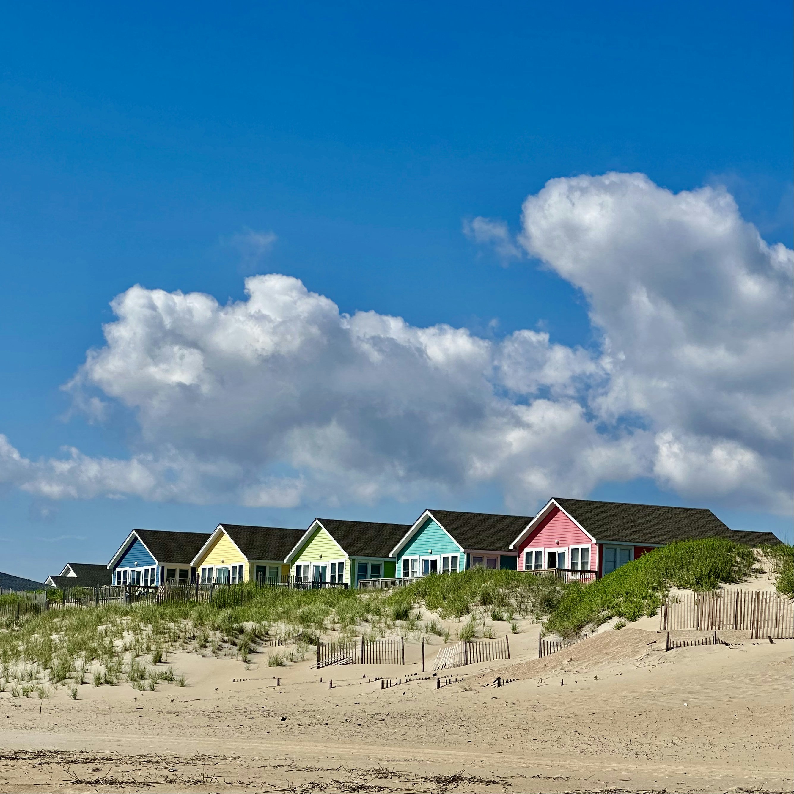 Colorful beach houses on a dune under blue sky.