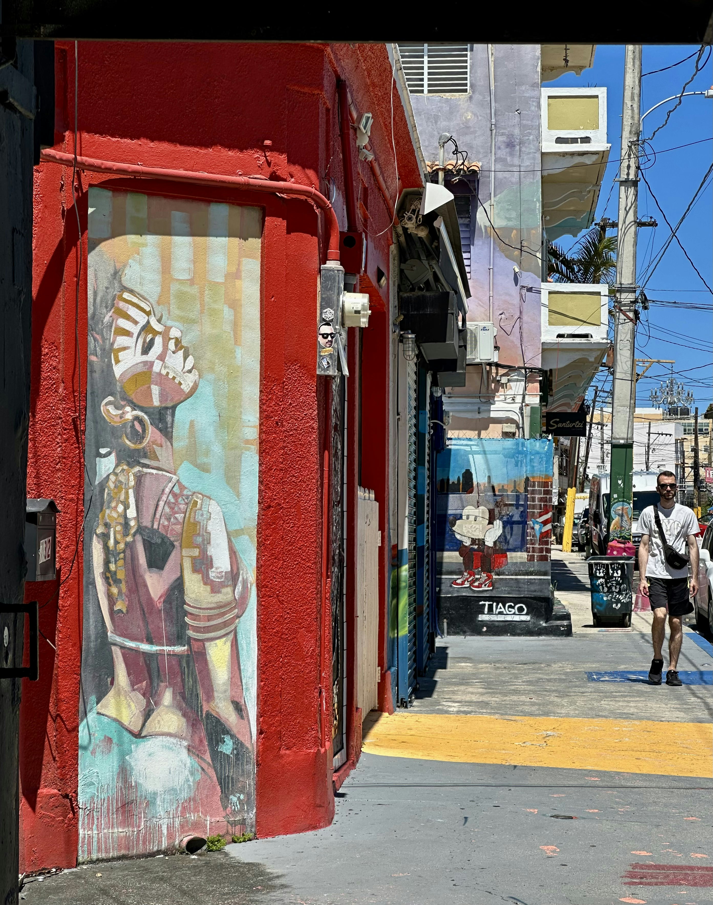 Man walks past colorful mural on red building
