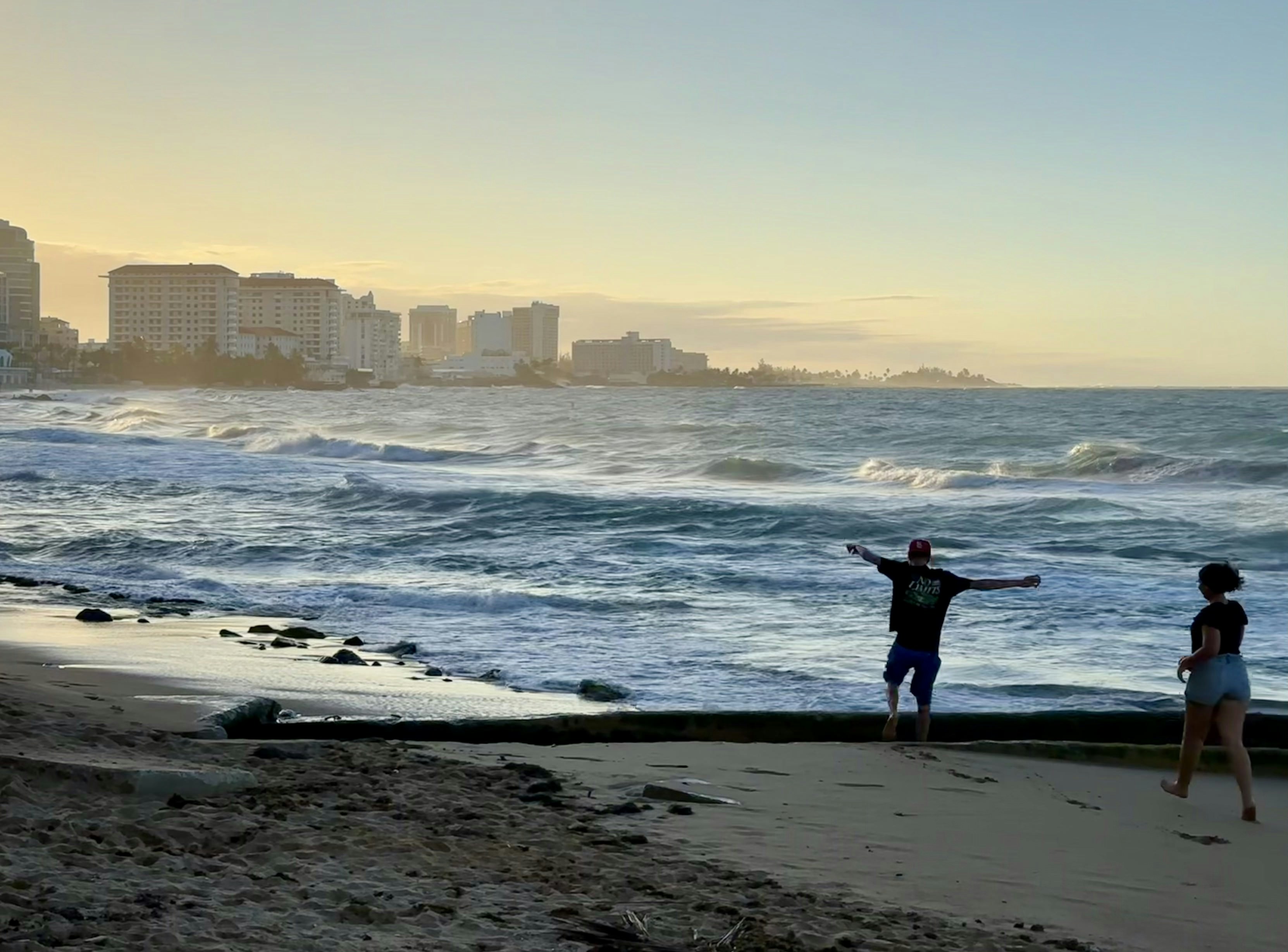 People on a beach with city skyline at sunset.