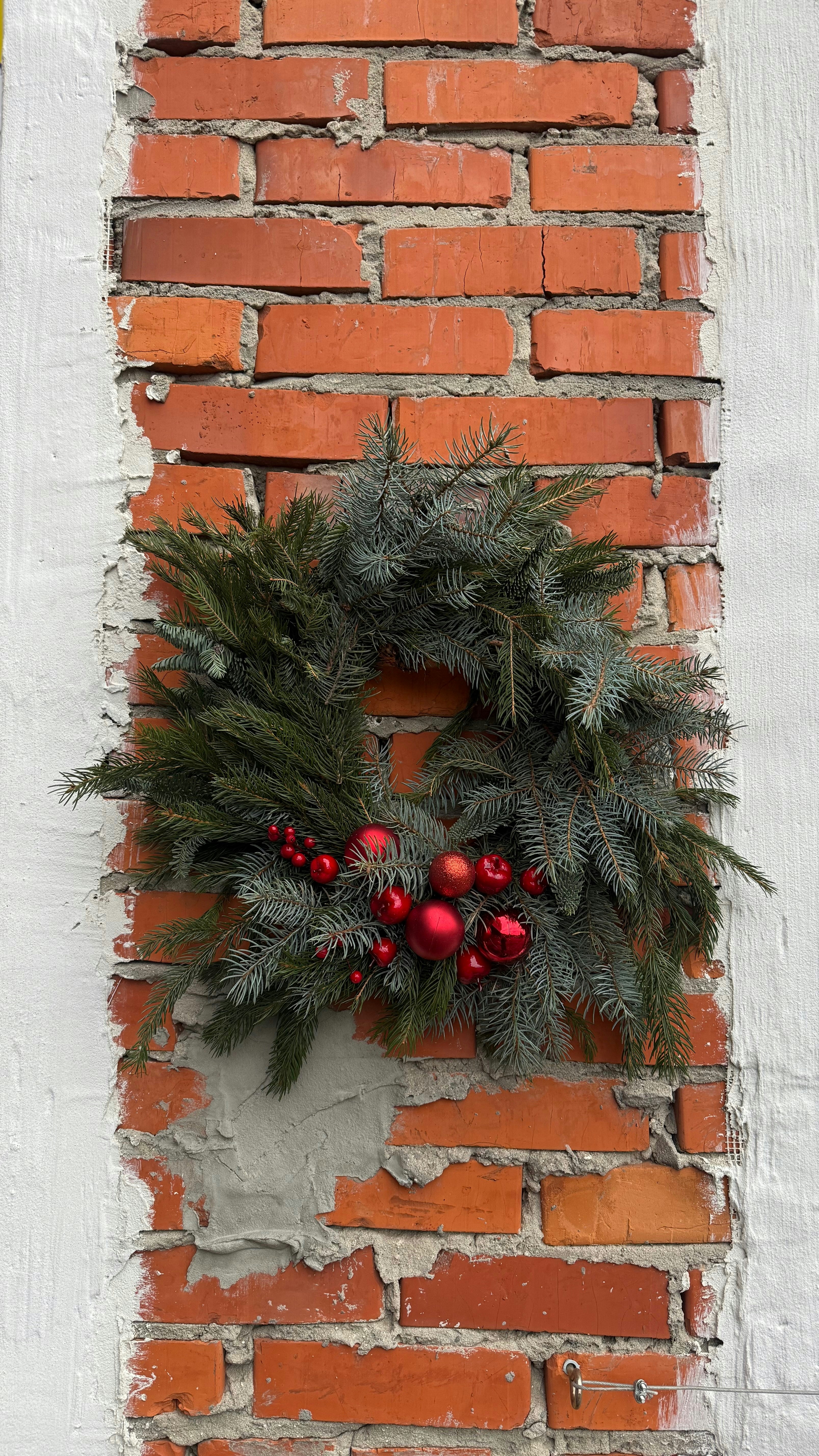 A christmas wreath with red ornaments on brick wall