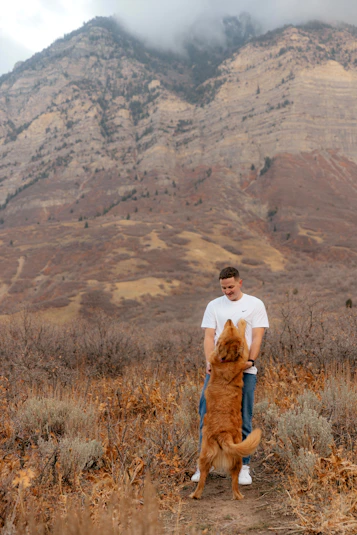 Man holding a golden retriever dog outdoors with mountains behind