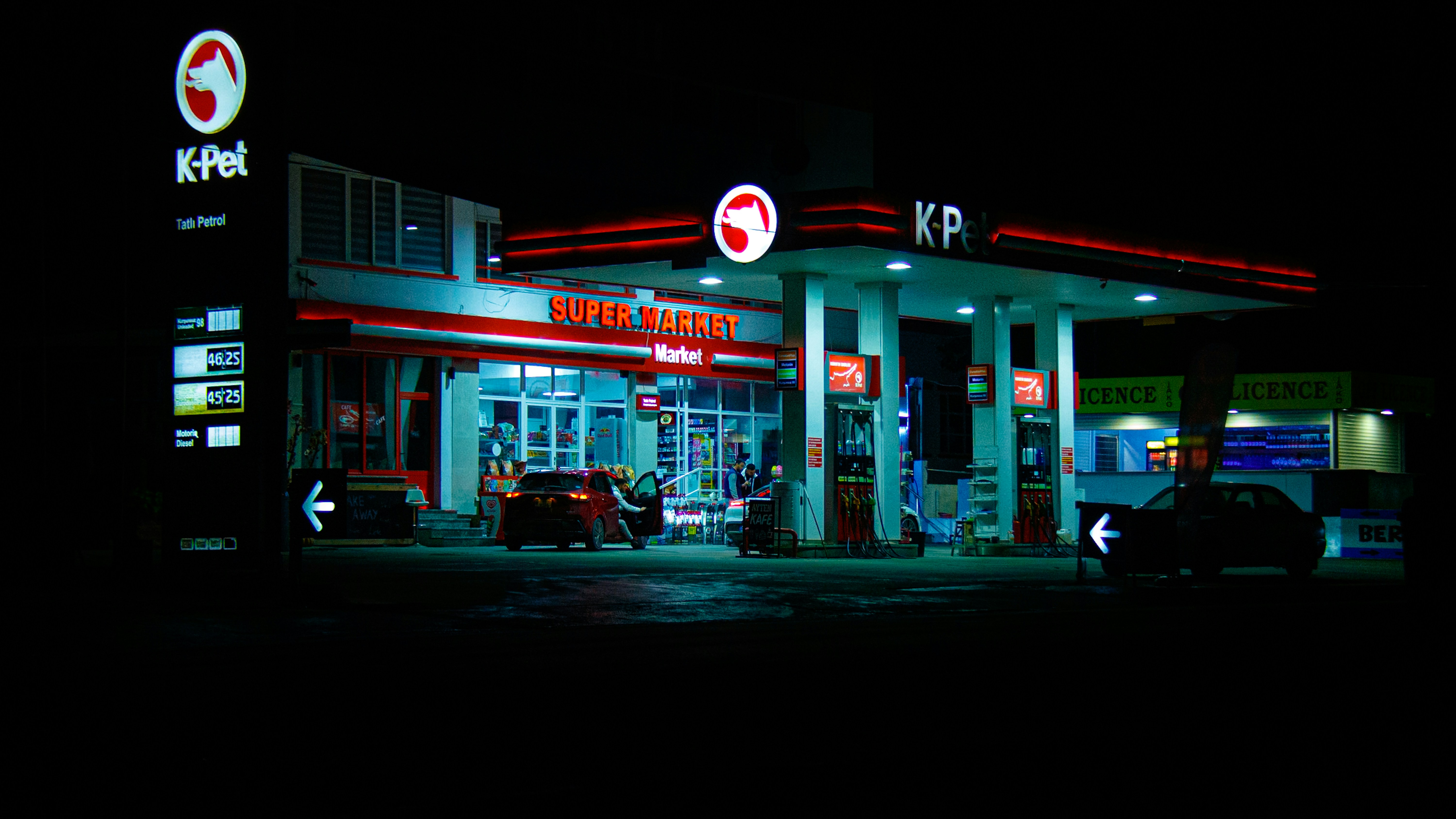 Gas station illuminated at night with cars present cars