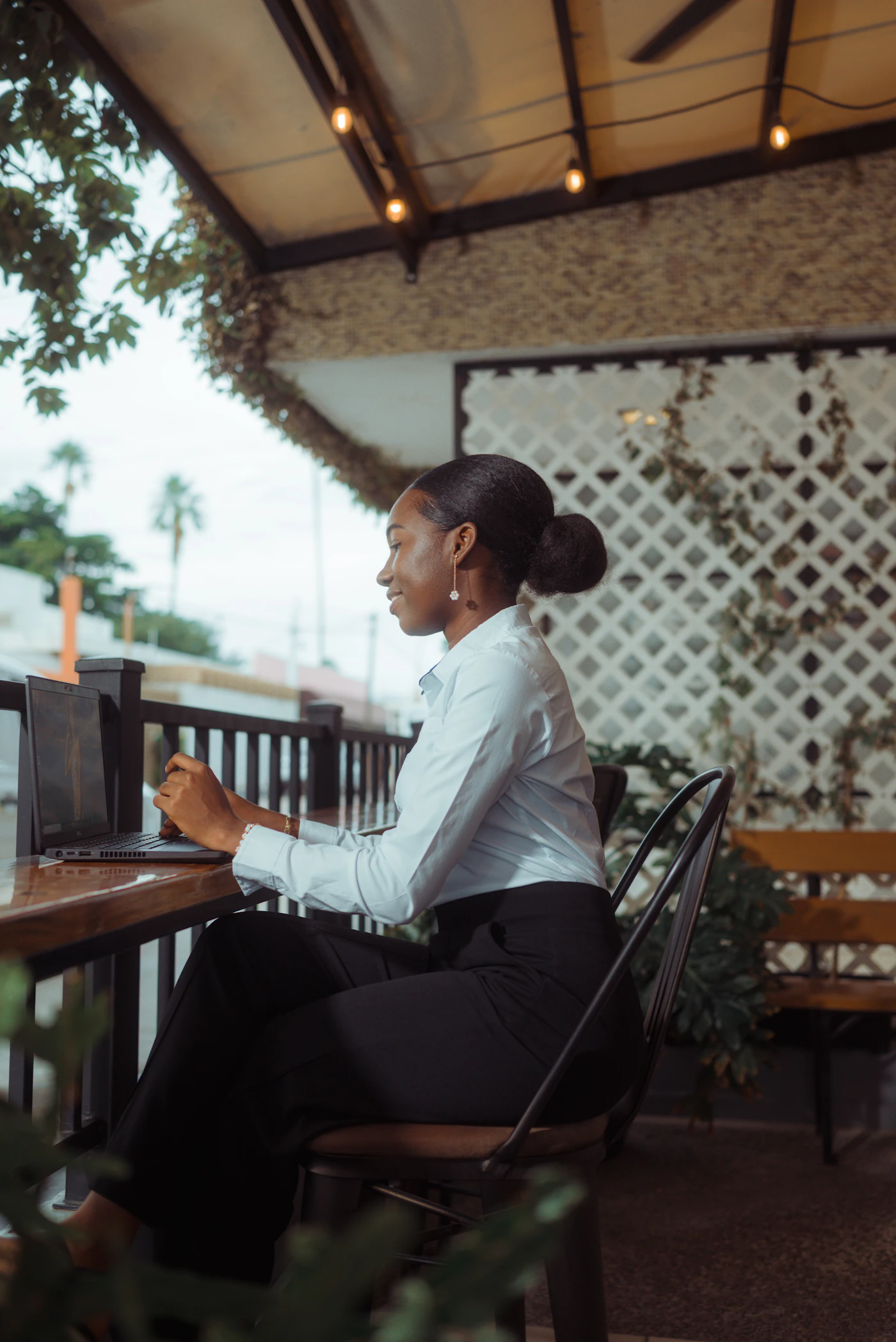 A woman working on her laptop at an outdoor cafe while reviewing designer portfolios