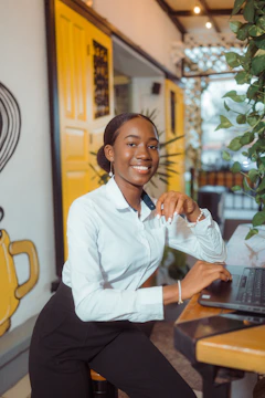 A smiling woman in a white shirt at a laptop.