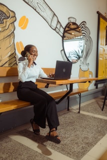 Woman on phone working on laptop at cafe