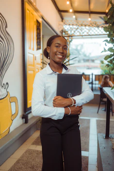 A woman in a white shirt holding a laptop in a cafe.