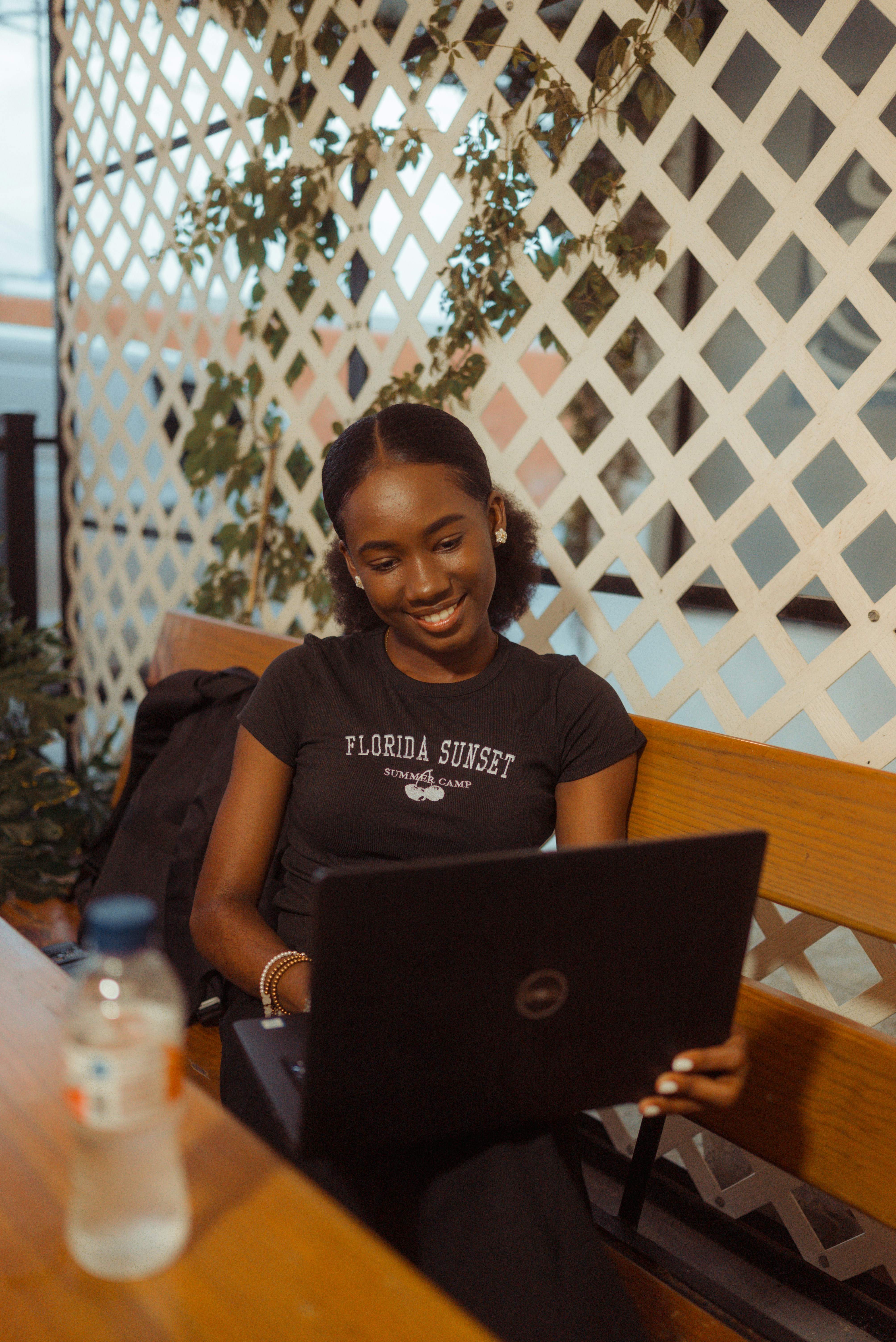 A woman in a black t-shirt using a laptop on a wooden bench