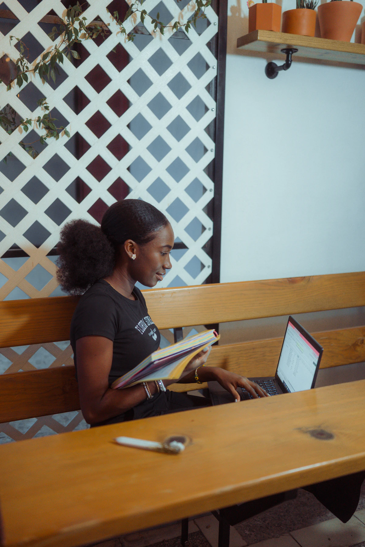 A woman in a black t-shirt working on a laptop at a wooden bench