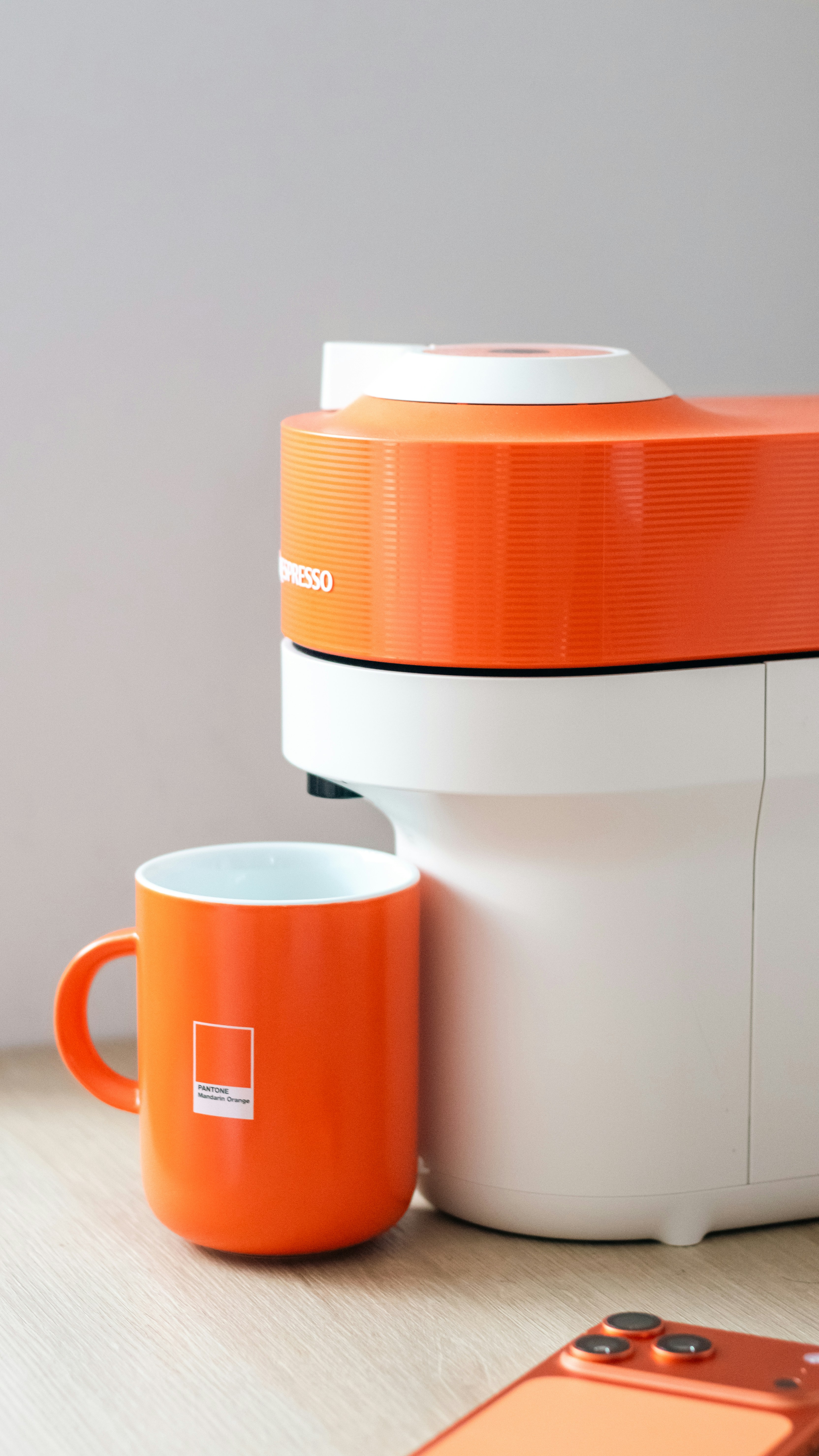 Orange mug next to a white and orange coffee machine.