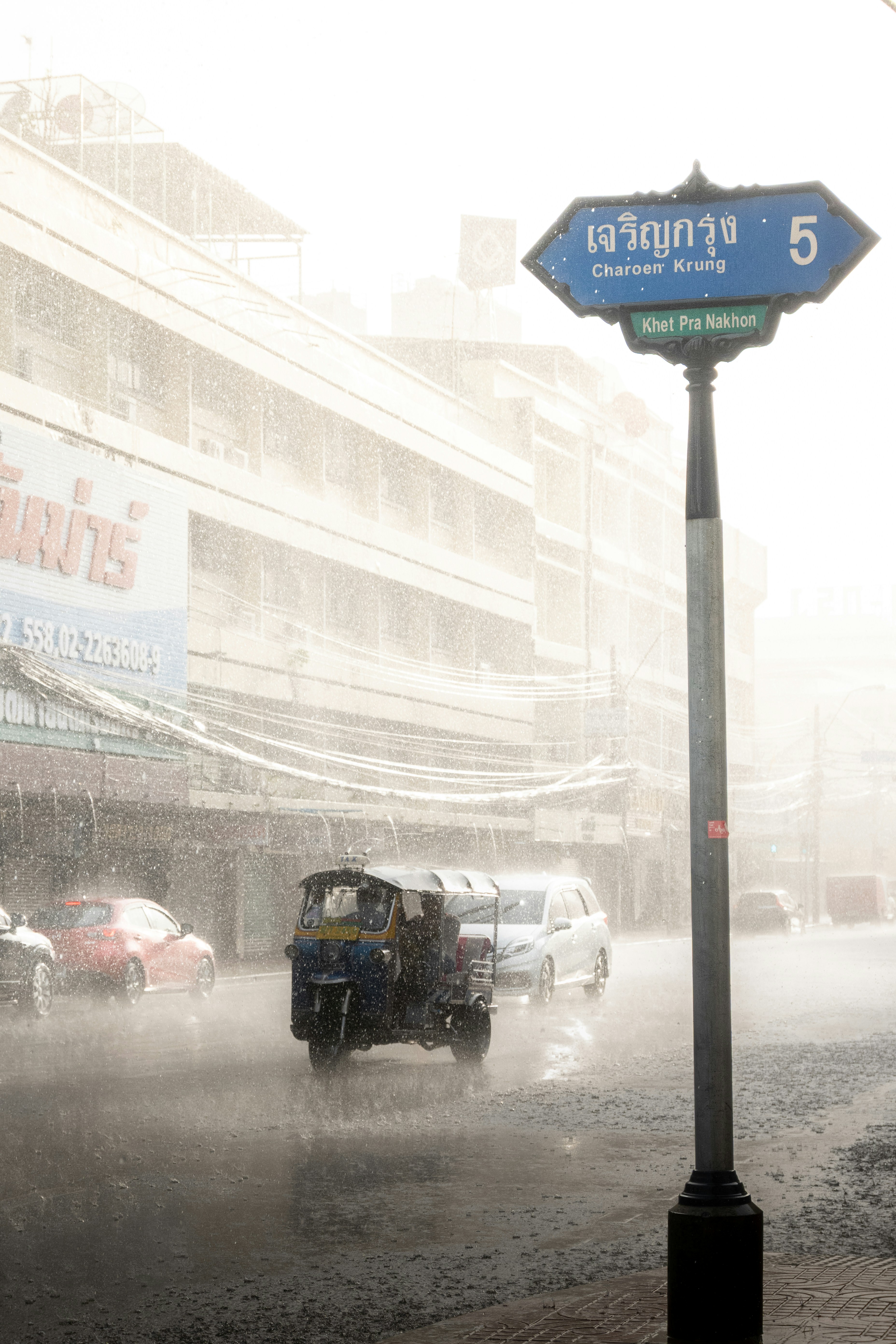 Tuk-tuk driving through heavy rain on city street.
