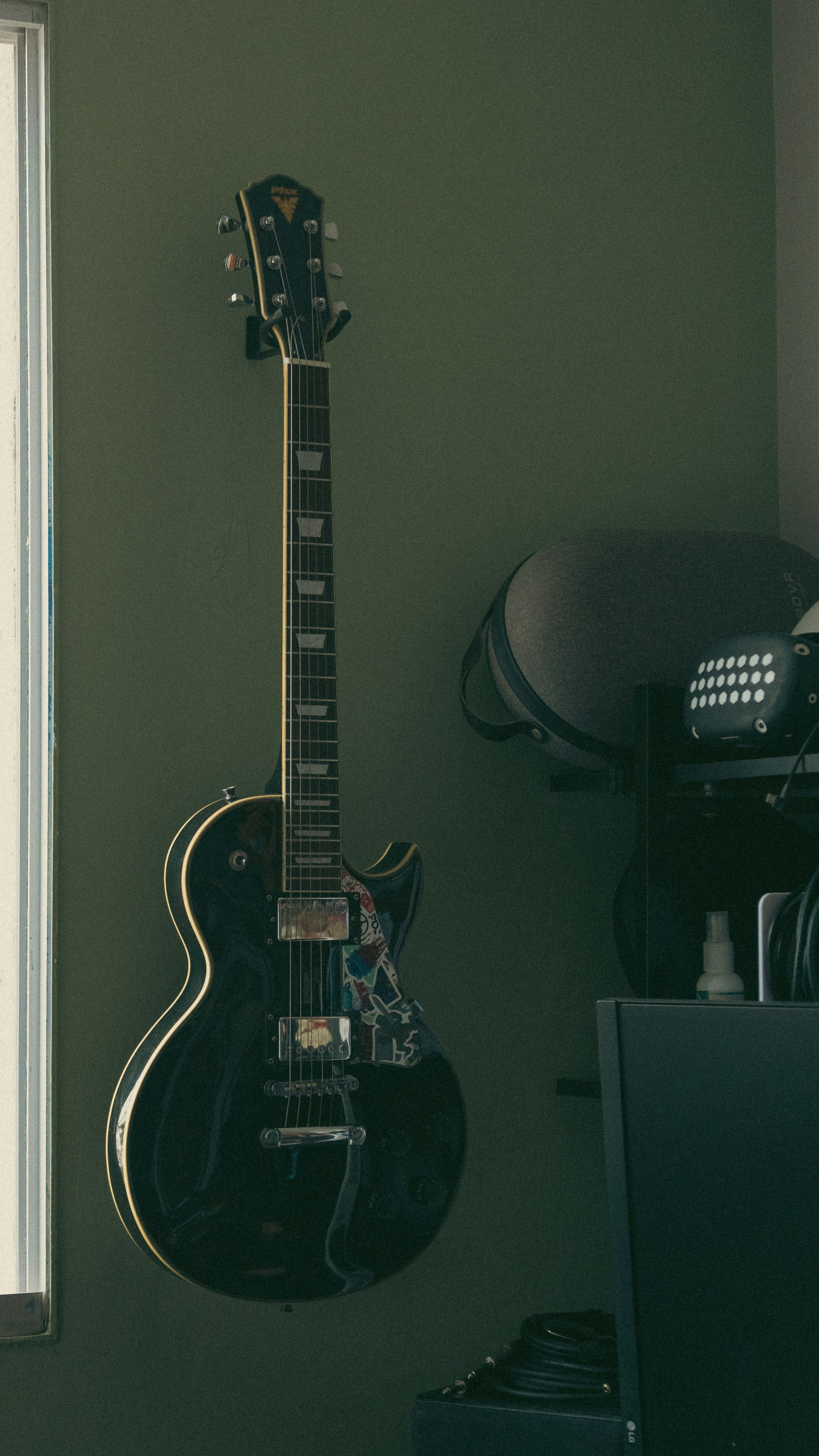 A black electric guitar hangs on a green wall.