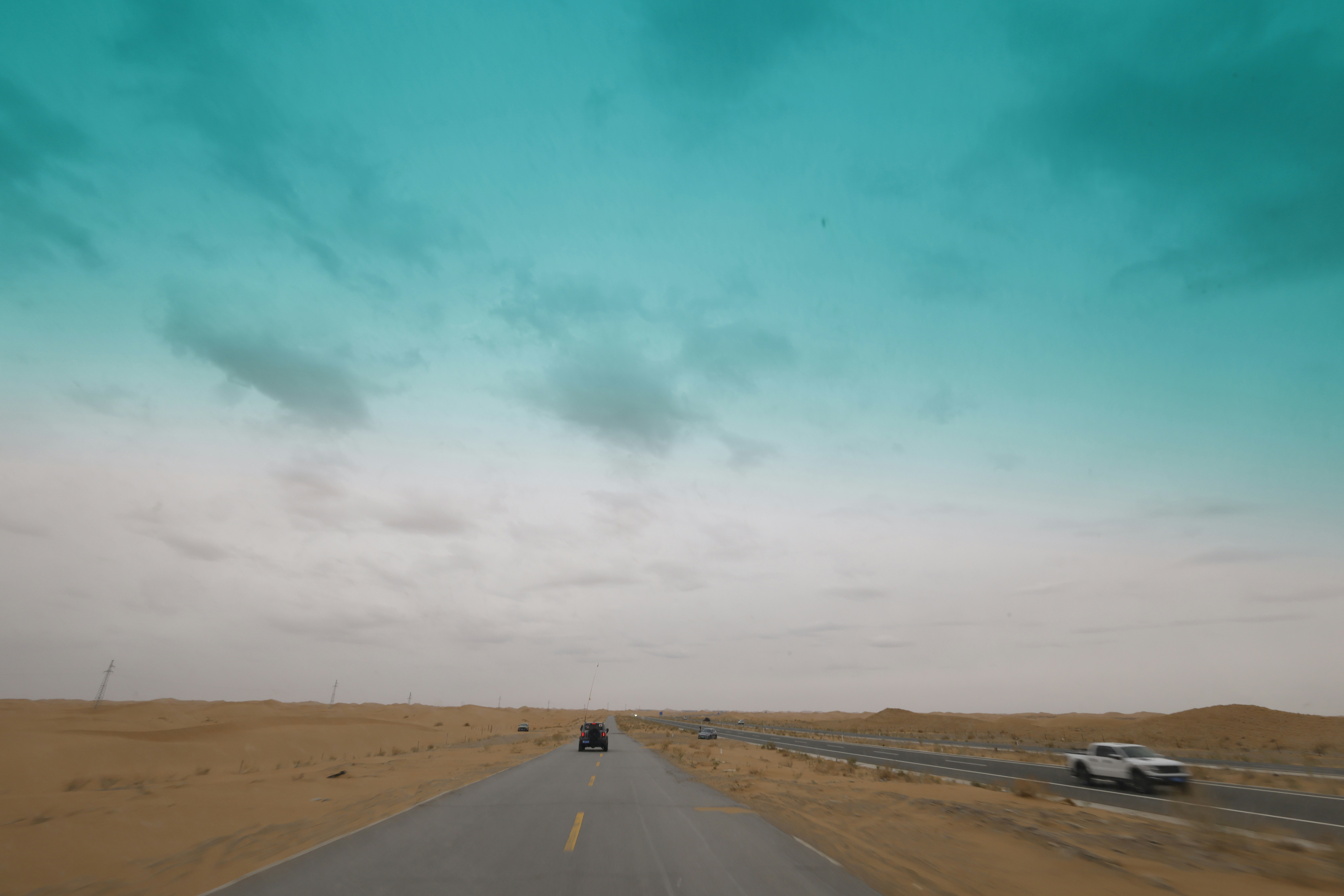 Cars driving on a desert road under a cloudy sky
