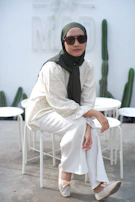 Woman in hijab and sunglasses sitting outdoors.