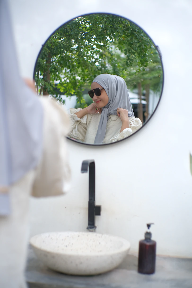 Woman in hijab smiles at her reflection in mirror.