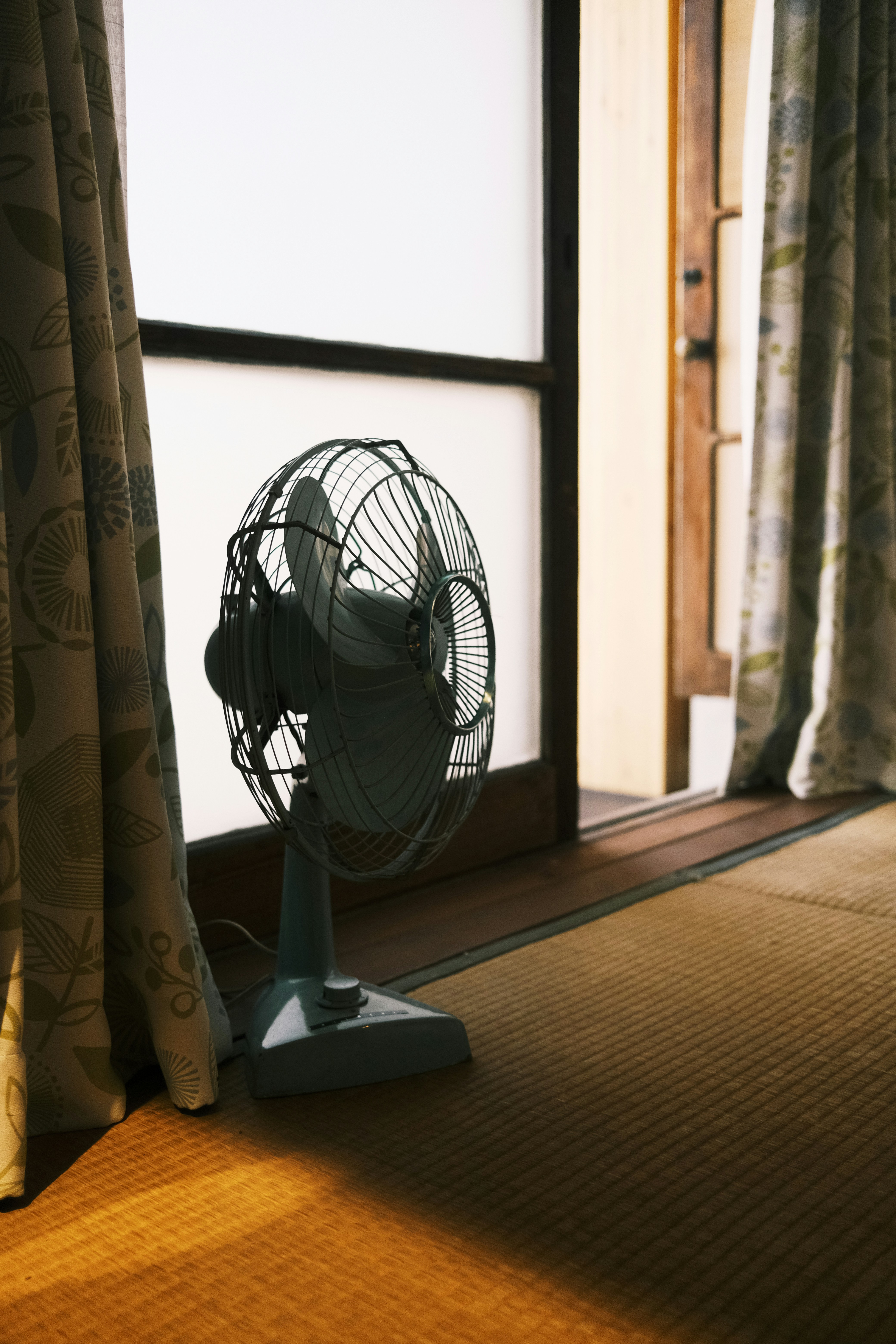 Un ventilador viejo está junto a una ventana soleada.