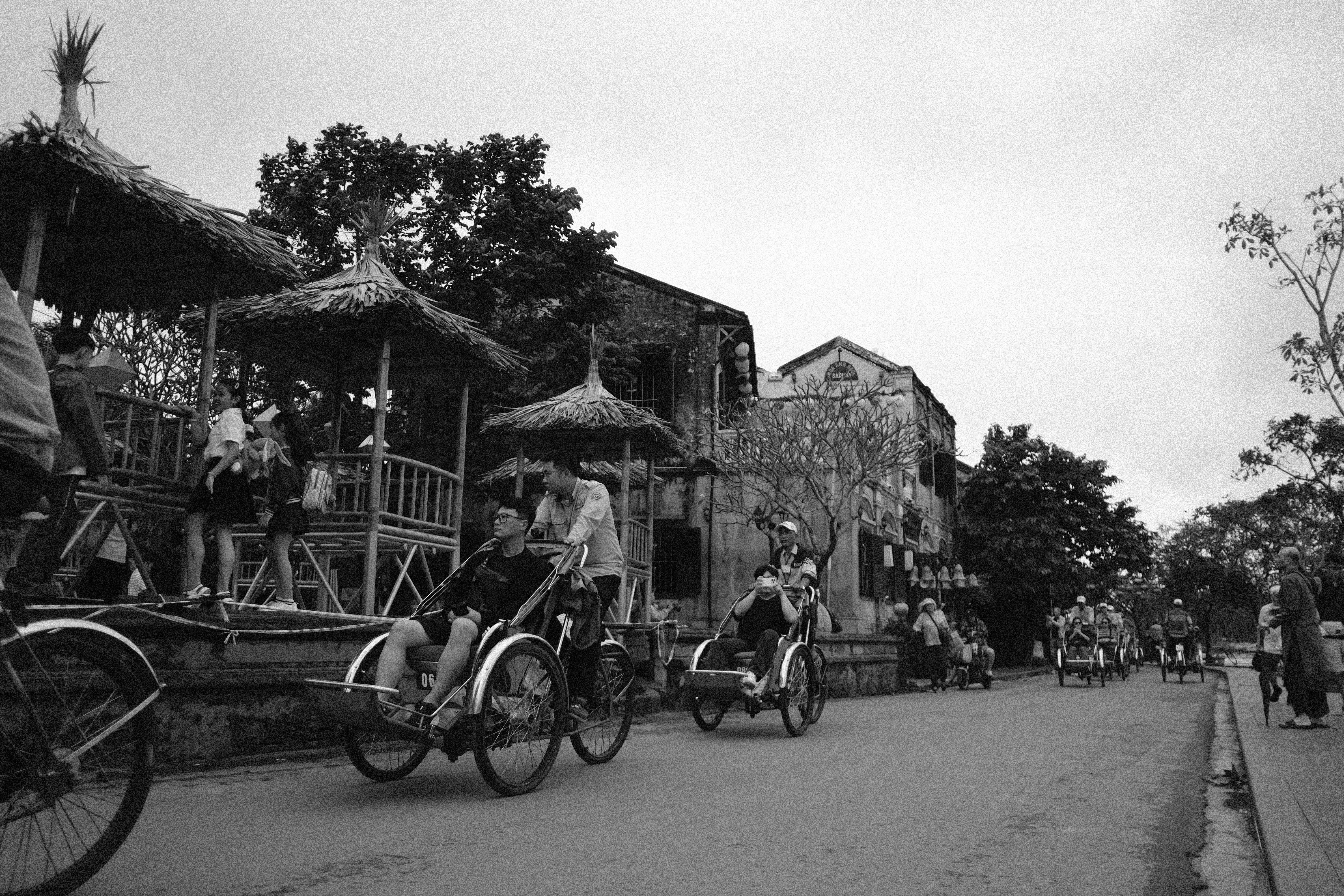 People riding cyclos on a street with buildings.
