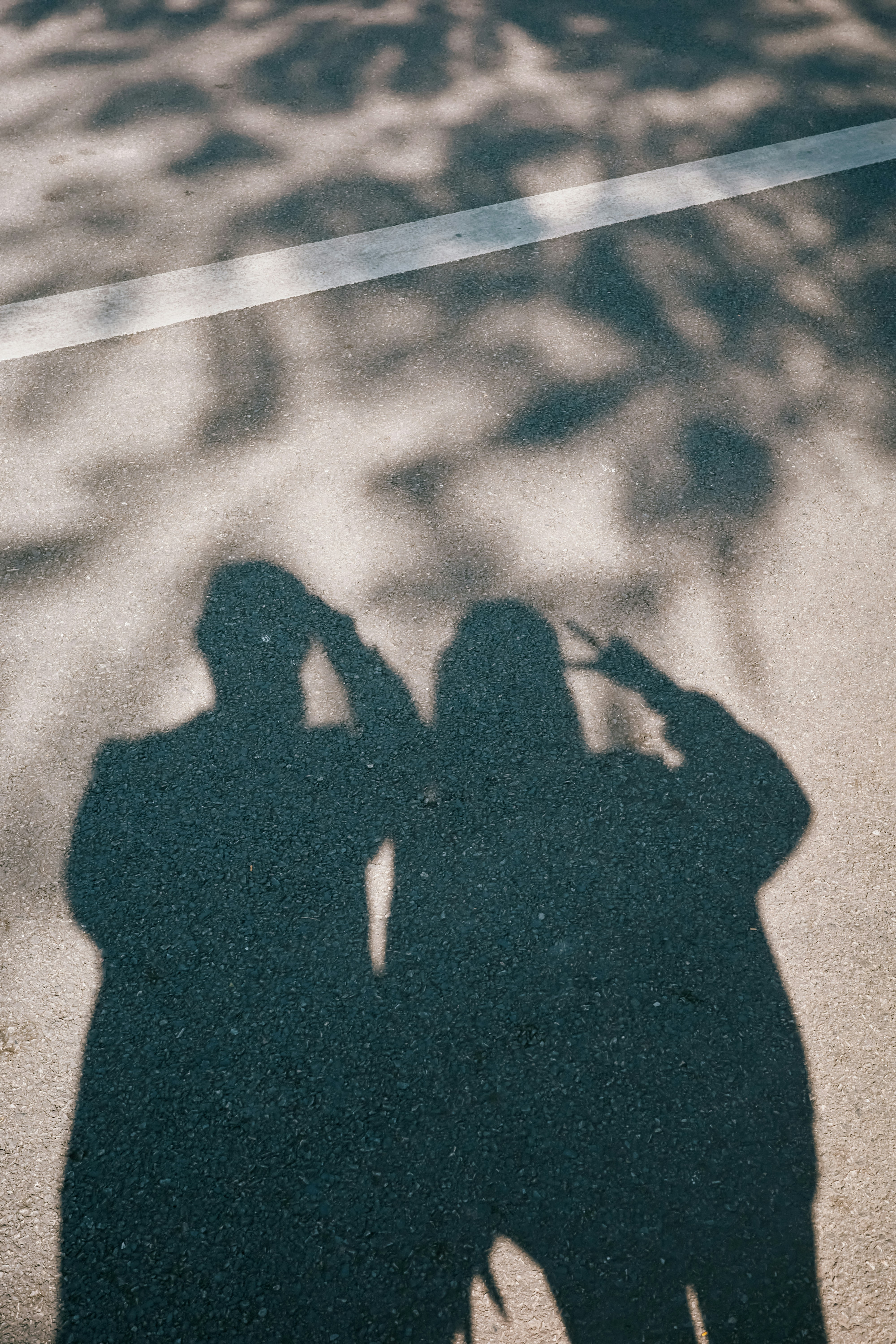 Shadows of two people on asphalt with a white line.