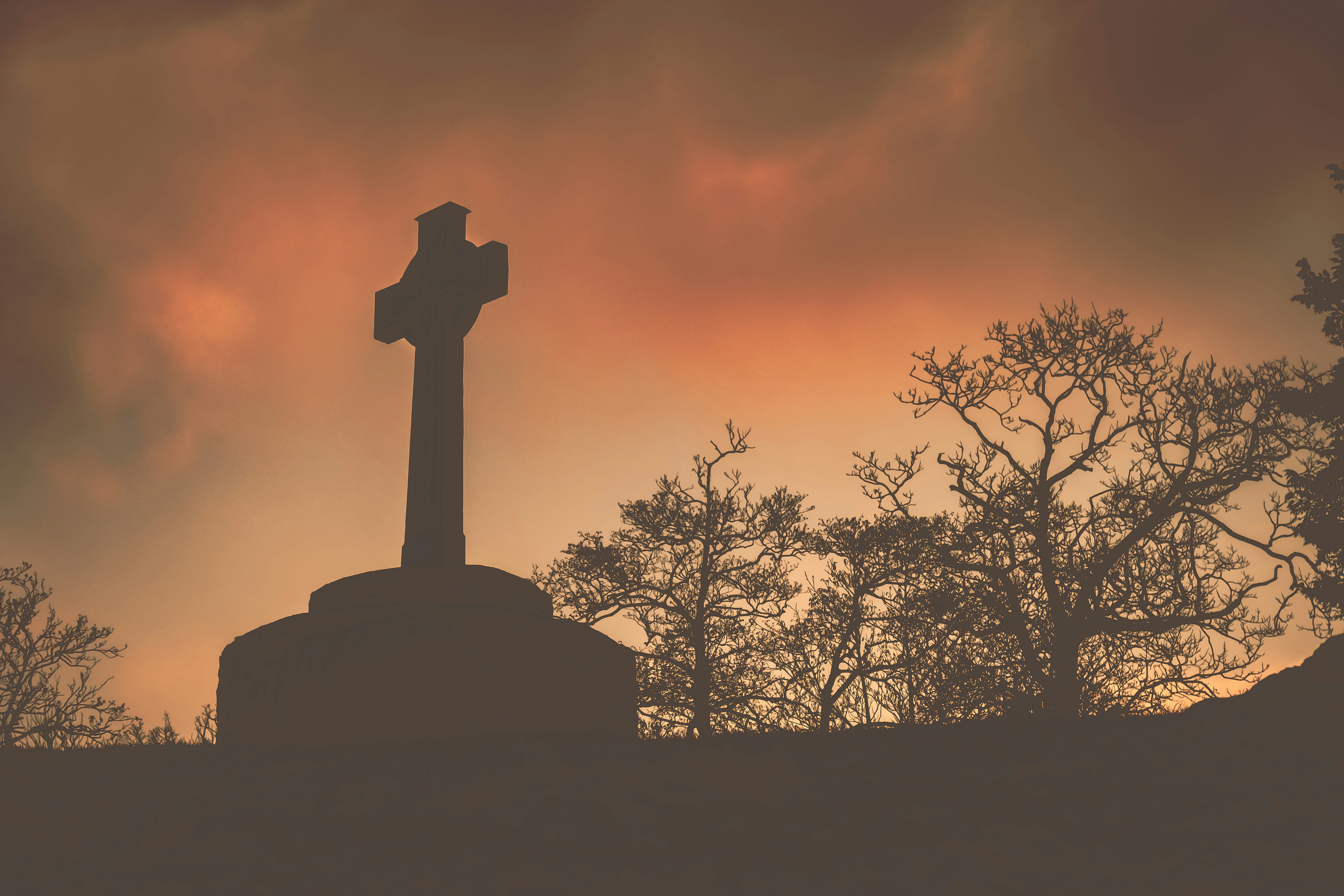 Silhouette of celtic cross against dramatic sunset sky
