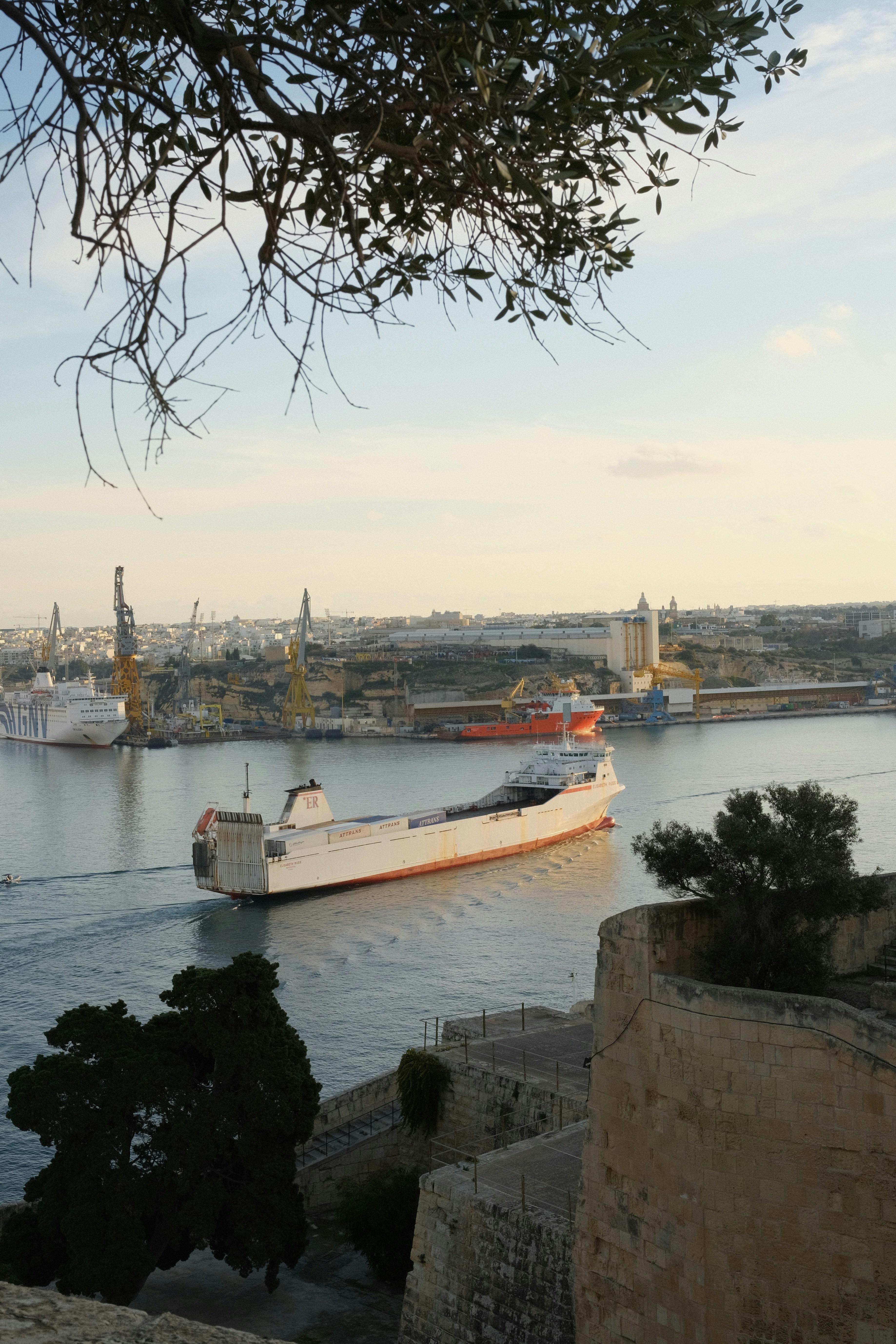 Ferry boat sailing in a large harbor with cranes.