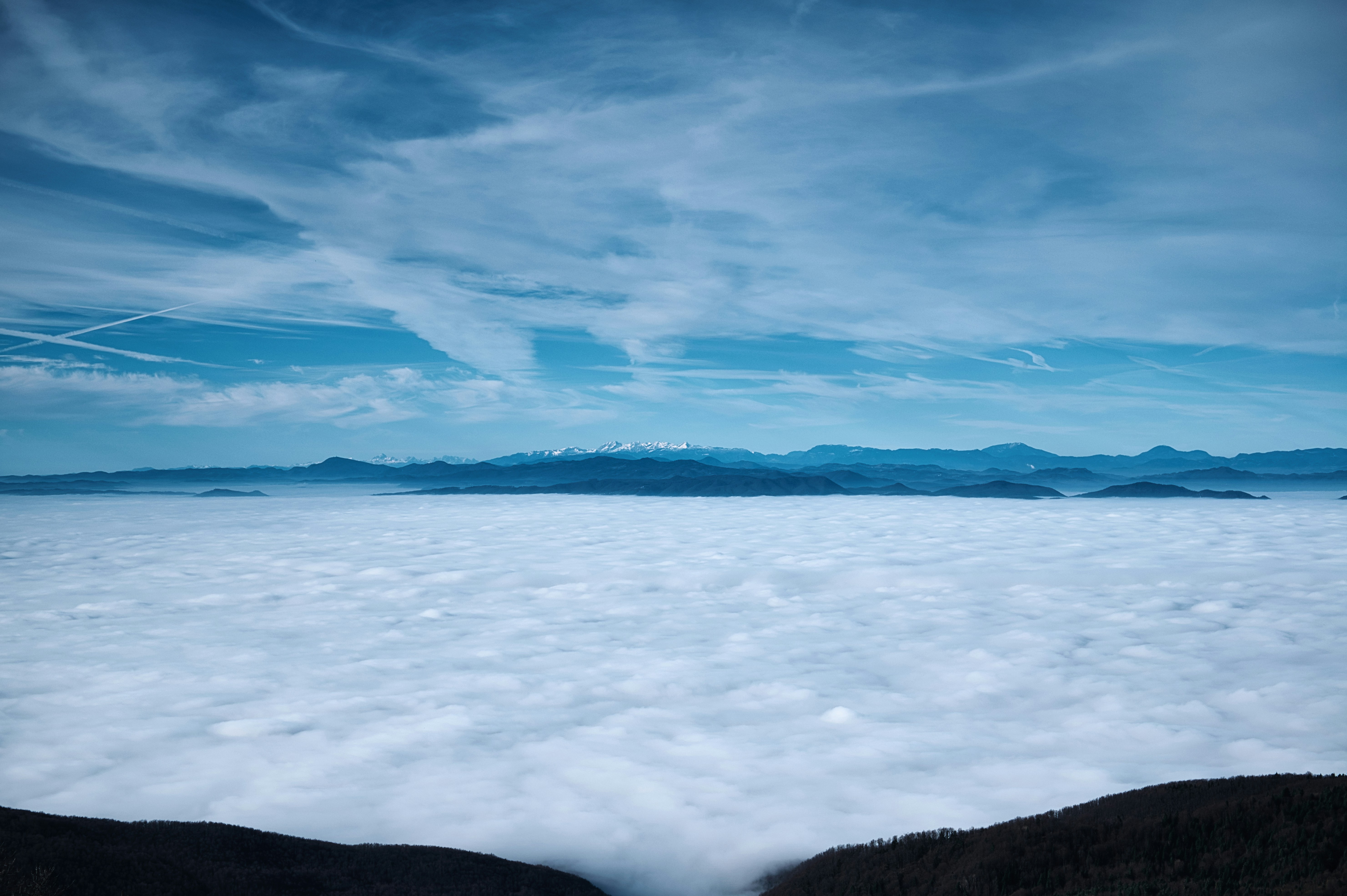 Sea of clouds with distant mountains under blue sky