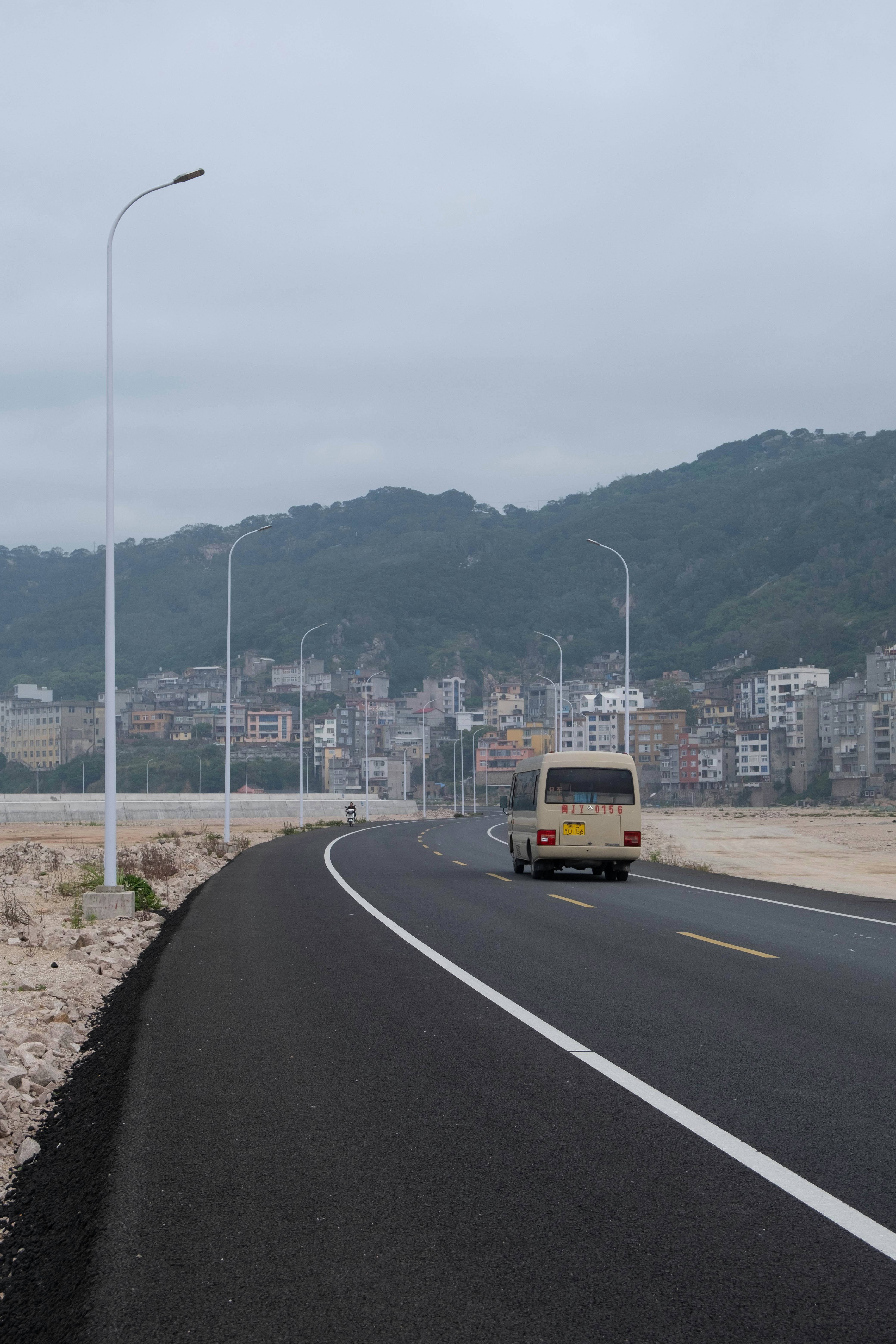 A van drives on a coastal road towards a town.