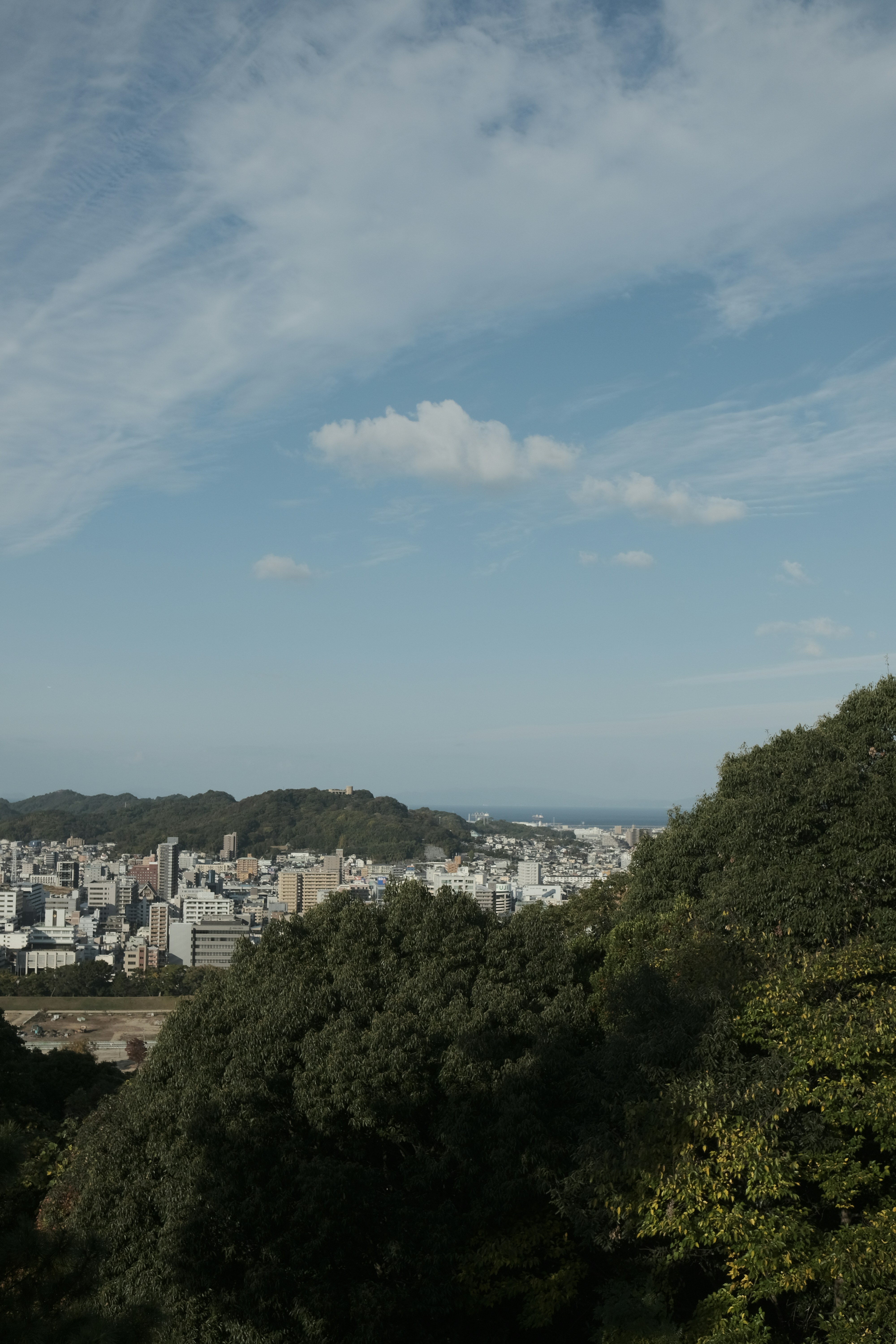 Cityscape nestled among green hills under a cloudy sky.